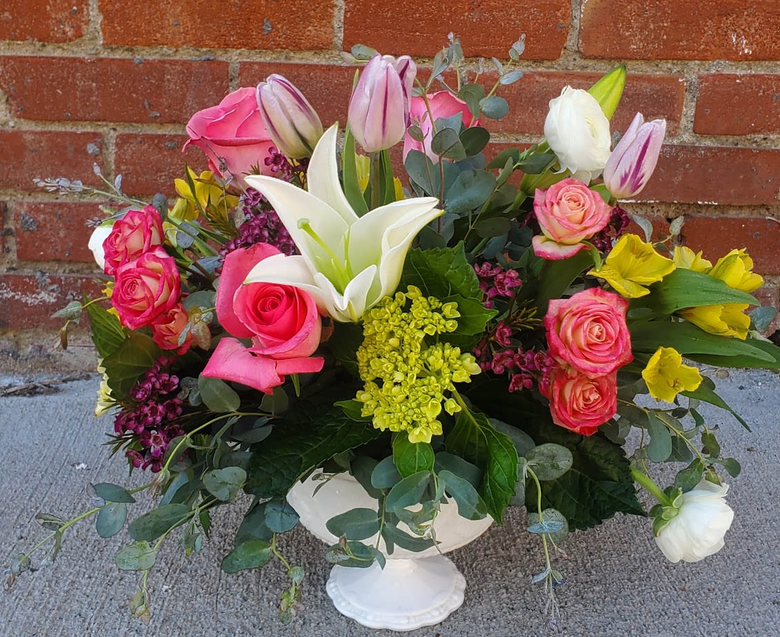 Grandma's Garden Grand Grandma's Garden Grand - This stunning flower arrangement is a harmonious blend of classic elegance and fresh, seasonal beauty. Lush, velvety roses in shades of soft blush, creamy ivory form the romantic heart of the bouquet. Nestled among them are graceful tulips, their smooth, curved petals adding a sense of movement and refined simplicity in hues of pastel pink, peach, and sunny yellow. Voluminous clusters of hydrangeas complete the arrangement. Set in a clear glass vase or an antique ceramic vessel, this arrangement is perfect for a wedding centerpiece, a thoughtful gift, or a statement piece for any elegant setting. Its palette and composition evoke timeless beauty and a gentle, uplifting charm.