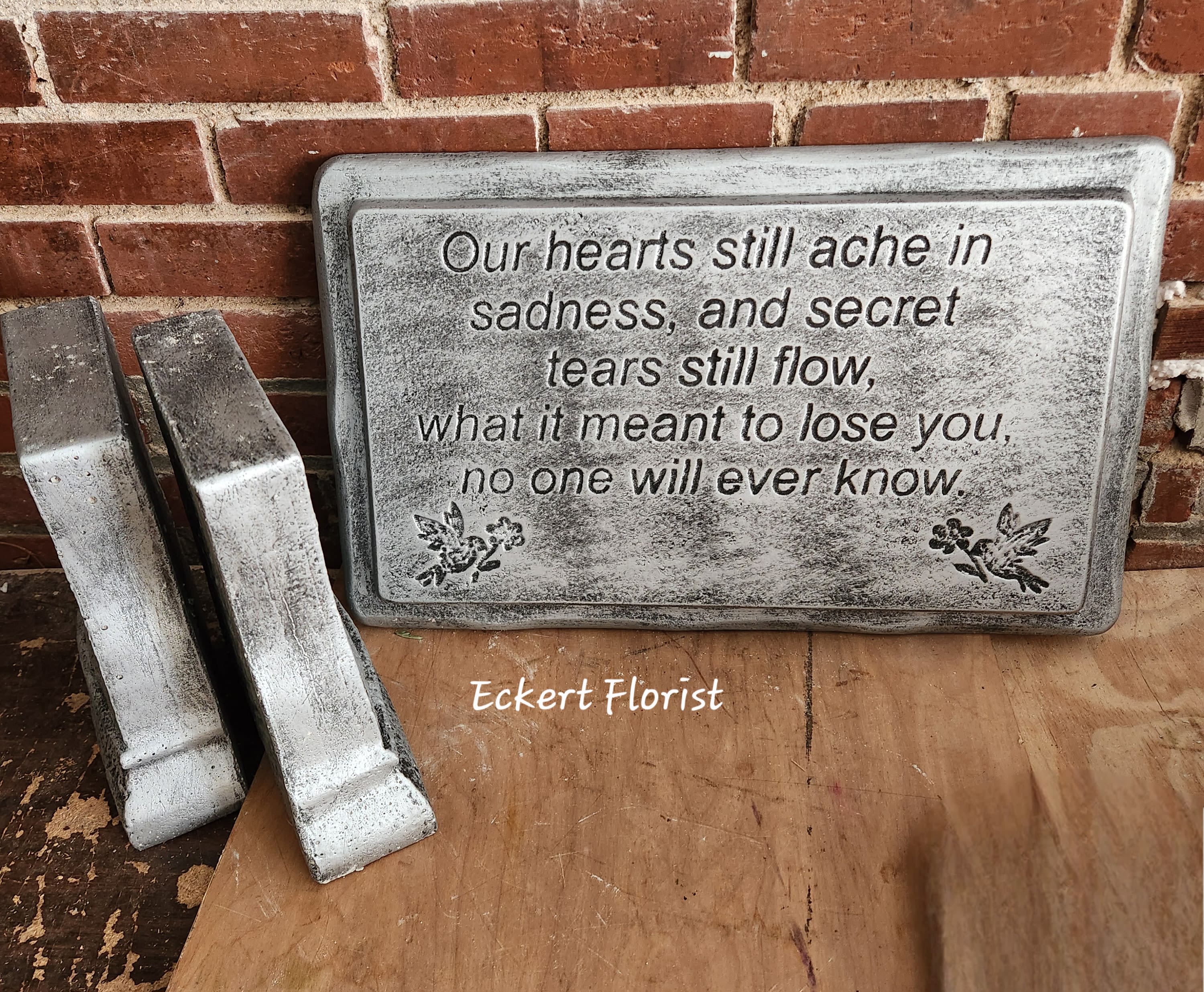 Eckert Florist's "Our Hearts Still Ache..." Stone Bench *Our Local Deliver Only Eckert Florist's "Our Hearts Still Ache..." Stone Bench *Our Local Deliver Only - Stone Garden Bench. Sentiment: "Our hearts still ache in sadness, and secret tears will flow, what it meant to lose you, no one will ever know." * LOCAL DELIVERY ONLY *Style of bench may vary. ALL OF OUR STONES COME DECORATED WITH A SHEER BOW, WILLOW, RAFFIA, AND OUR SIGNATURE BIRD.