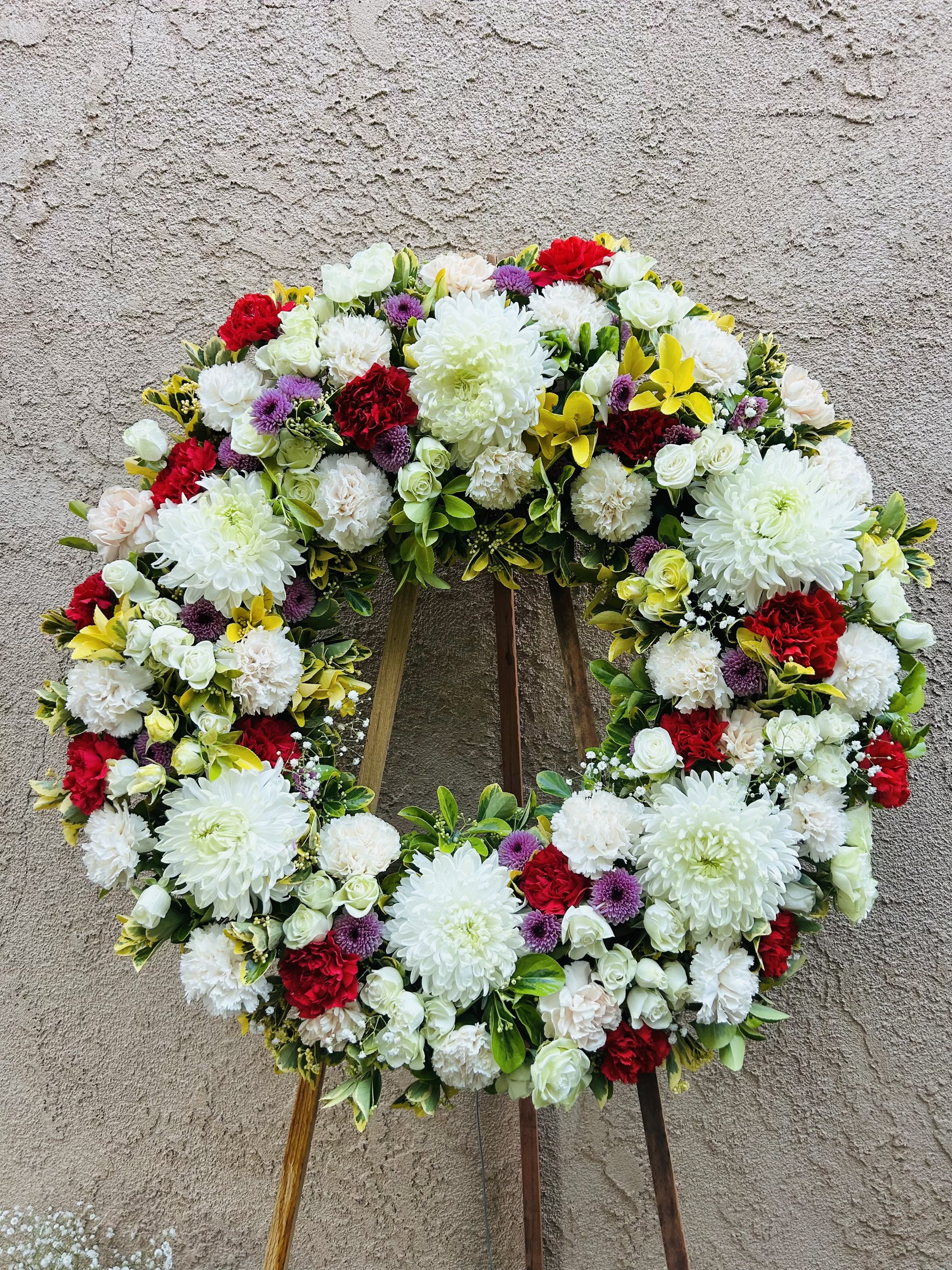 Legacy  - Beautiful funeral spray wreath featuring white chrysanthemums, yellow roses, pink carnations, and red carnations with green accents.