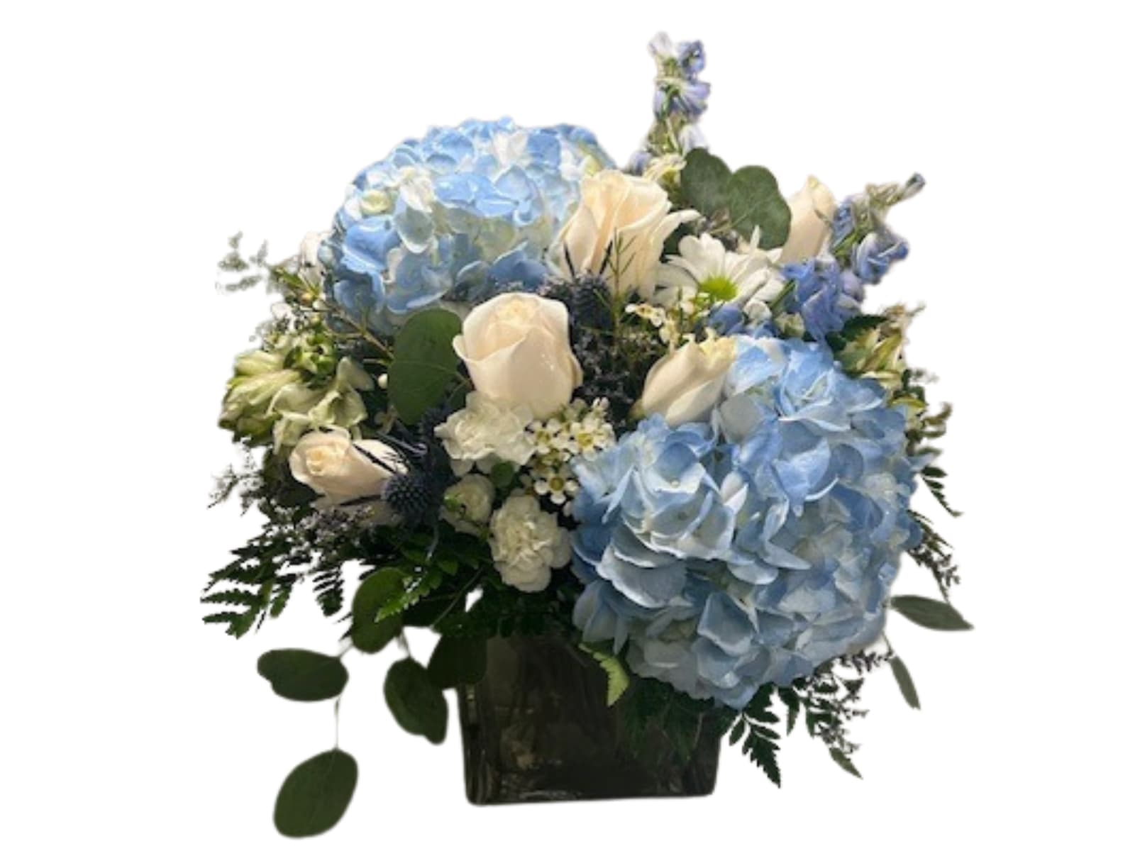 Blue Skies Blue Skies - Large mound style arrangement in cube featuring blue hydrangeas, roses, eucalyptus, and filler. This piece makes the perfect give to cheer someone up, or can be used as a centerpiece.