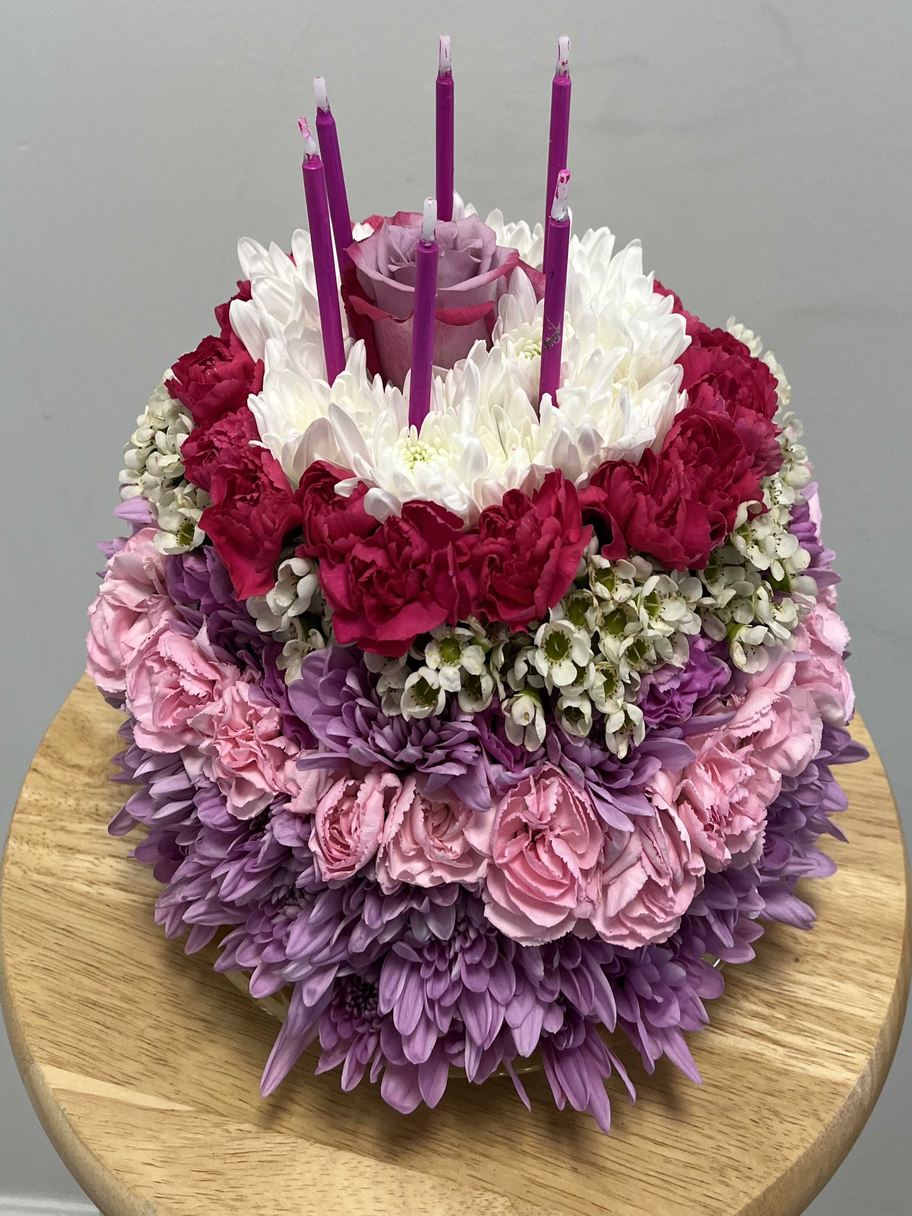 Birthday Cake Birthday Cake - This arrangement features lavender chrysanthemums, pink mini carnations, white wax, hot pink carnations and white chrysanthemums. Topped with lavender candles and a lavender rose, this arrangement is perfect for any celebration.