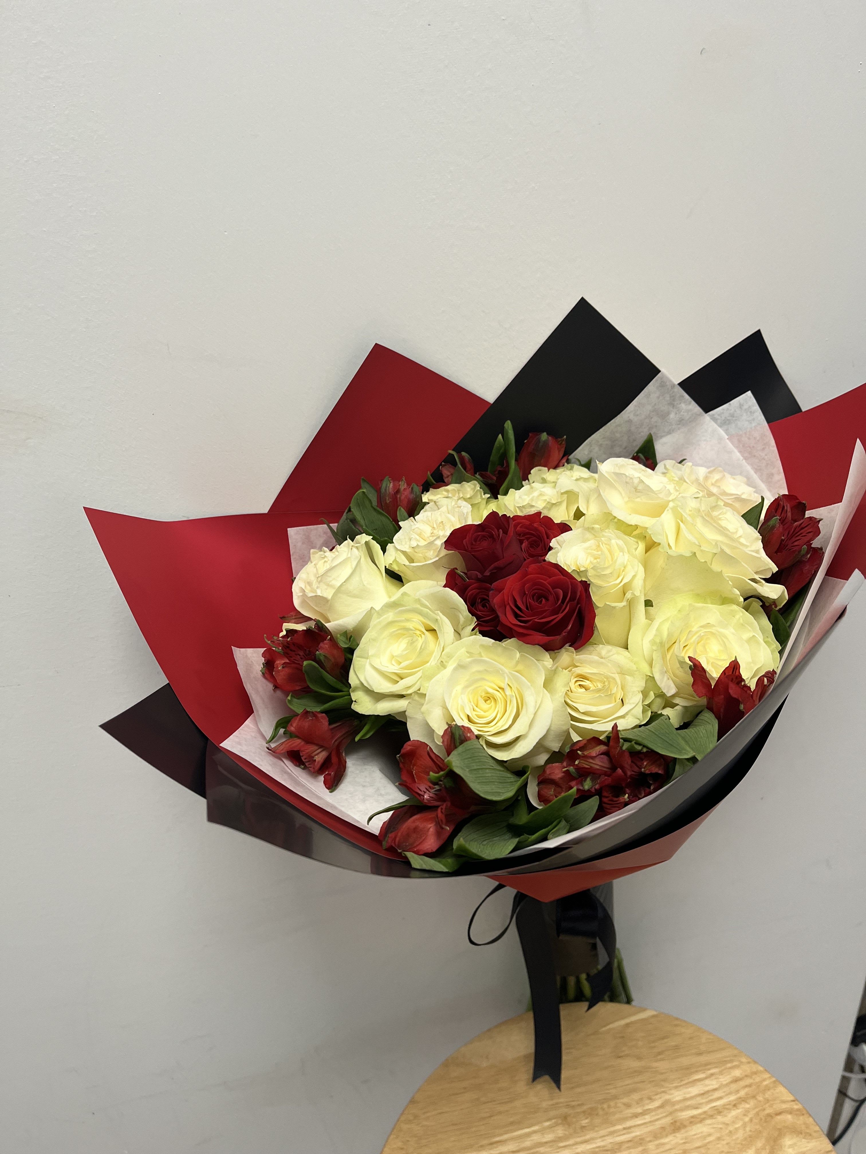 Crimson Elegance Crimson Elegance - This bouquet features deep red roses surrounded by pale white roses and red alstroemeria. Wrapped in red, black and white paper with a black ribbon, this bouquet is perfect for sleek luxurious presentation - ideal for anniversaries, romantic gestures, or elegant celebrations.