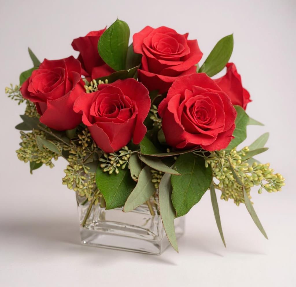AMORE IN ANTICIPO - &quot;Amore in Anticipo&quot; features half a dozen exquisite red Ecuadorian roses arranged in a sleek glass cube, accented with lush seeded eucalyptus. A perfect expression of love and anticipation, this compact design radiates elegance and romance.. 