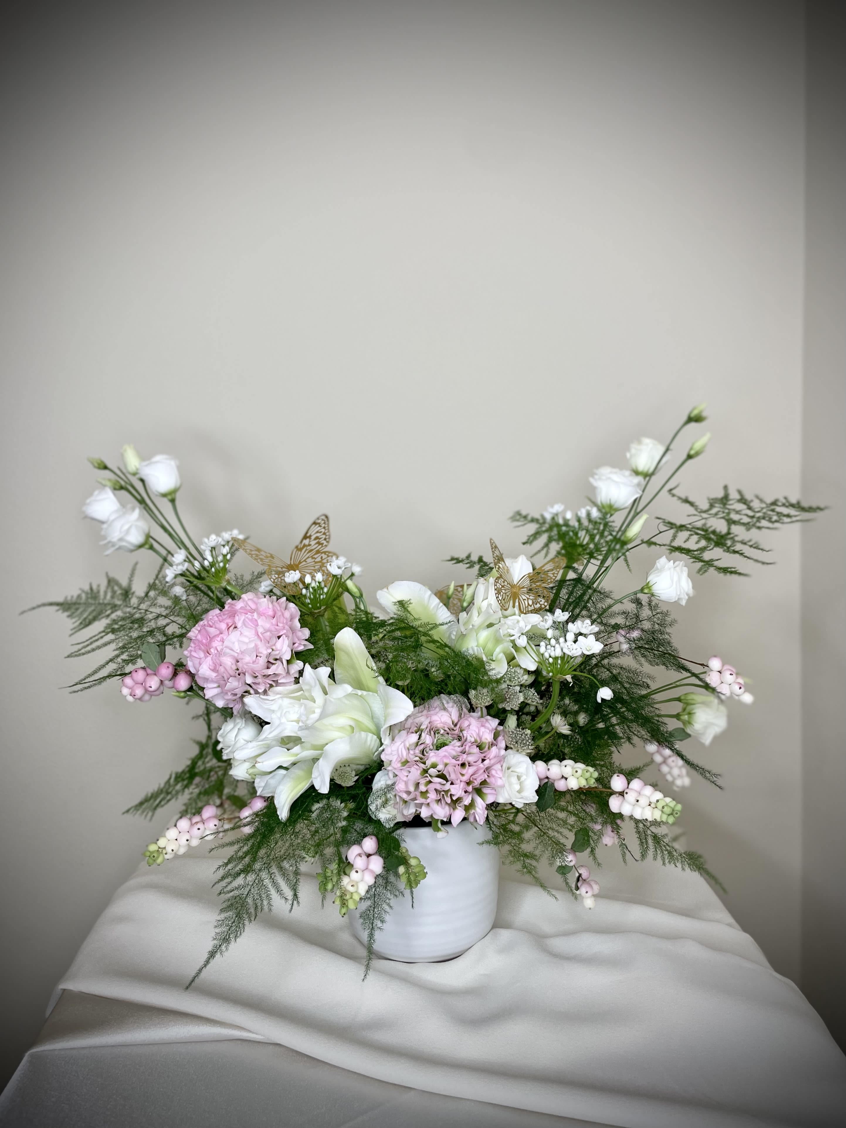 Ma Chérie  - My dear, or Ma Chérie, commands attention in its whimsical shape.  Light pinks and bright whites bring a sheer sense of innocence in this fun arrangement made to add flair into its surroundings.  This arrangement features artfully arranged premium flowers placed into a foam free frog pin in a white ceramic vase.  Finished with fluttering butterflies, this arrangement is sure to bring a smile to all in its presence. 