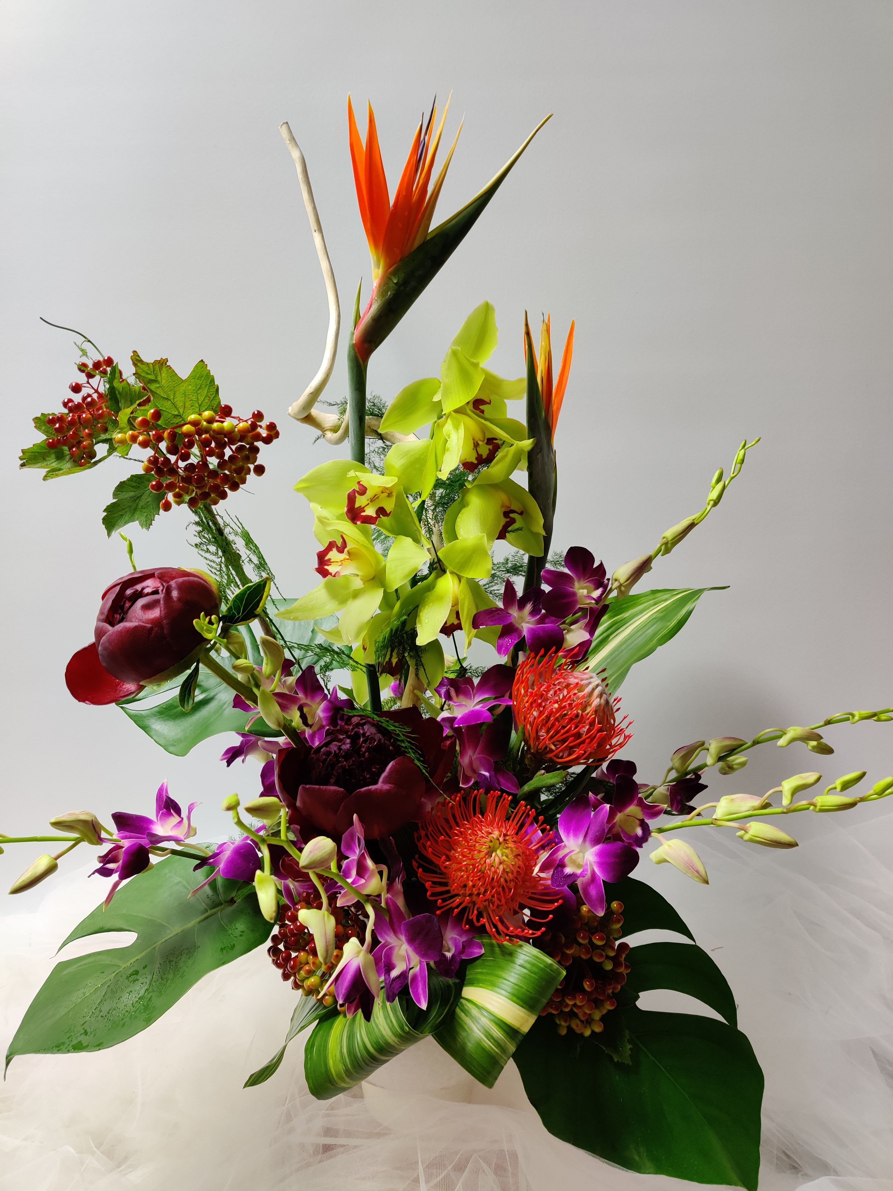 Lush Mirage - Here is another one of our beautiful Ikebana style arrangements made with cymbidium orchids, birds of paradise, pin cushions, peonies, orchids, berries, and elegant assorted greens.