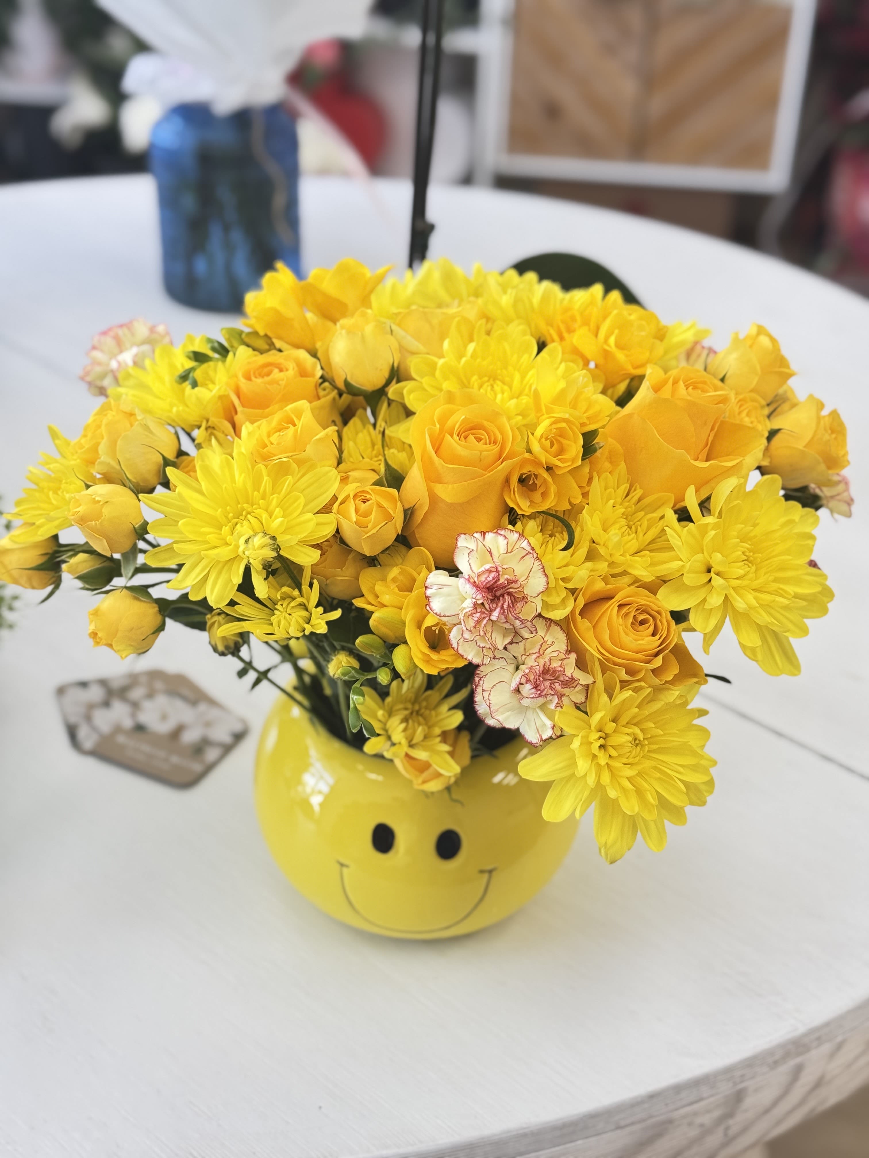 Lemonade Flowers - Send smiles and sunshine with our Smiley Sunshine Bouquet! Designed in a bright yellow smiley-face vase, this happy arrangement features a vibrant mix of golden yellow roses, cheerful chrysanthemums, miniature spray roses, and delicate carnations. It’s the perfect floral gift to brighten someone’s day, whether it's for a birthday, get well soon, thank you, or just because.
