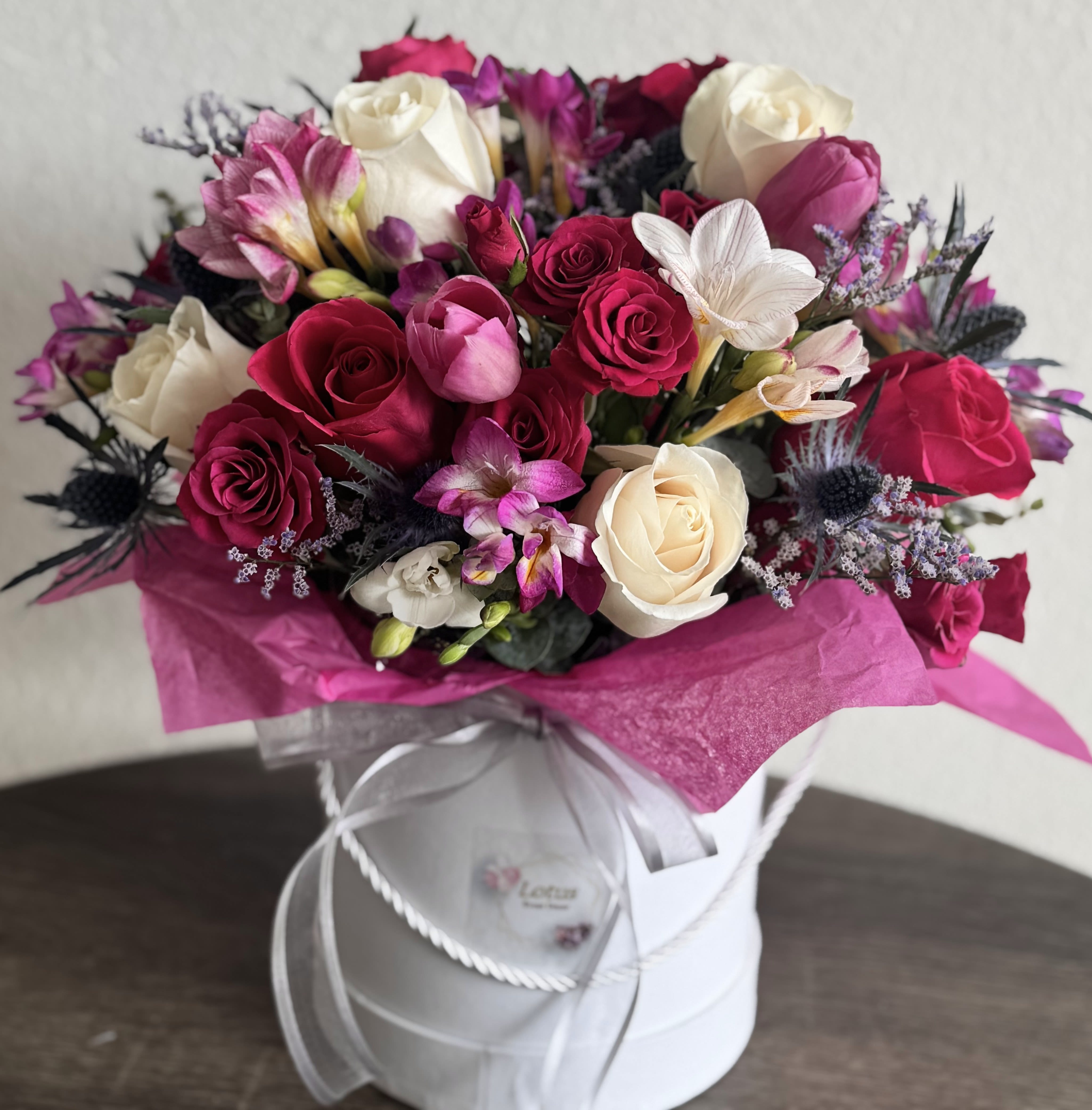 Elegant Romance Floral Box - Make a statement with this lush and romantic floral arrangement designed in a pristine white hat box, wrapped in luxurious satin ribbons. Featuring a harmonious blend of velvety red roses, creamy ivory roses, deep pink spray roses, exotic orchids, alstroemeria, and whimsical thistles, this bouquet is both classic and contemporary.  Each bloom is thoughtfully chosen for color, texture, and elegance — making this piece a perfect gift for anniversaries, birthdays, Valentine's Day, or any moment you want to feel unforgettable. Handcrafted with love by our floral artisans in Los Angeles.