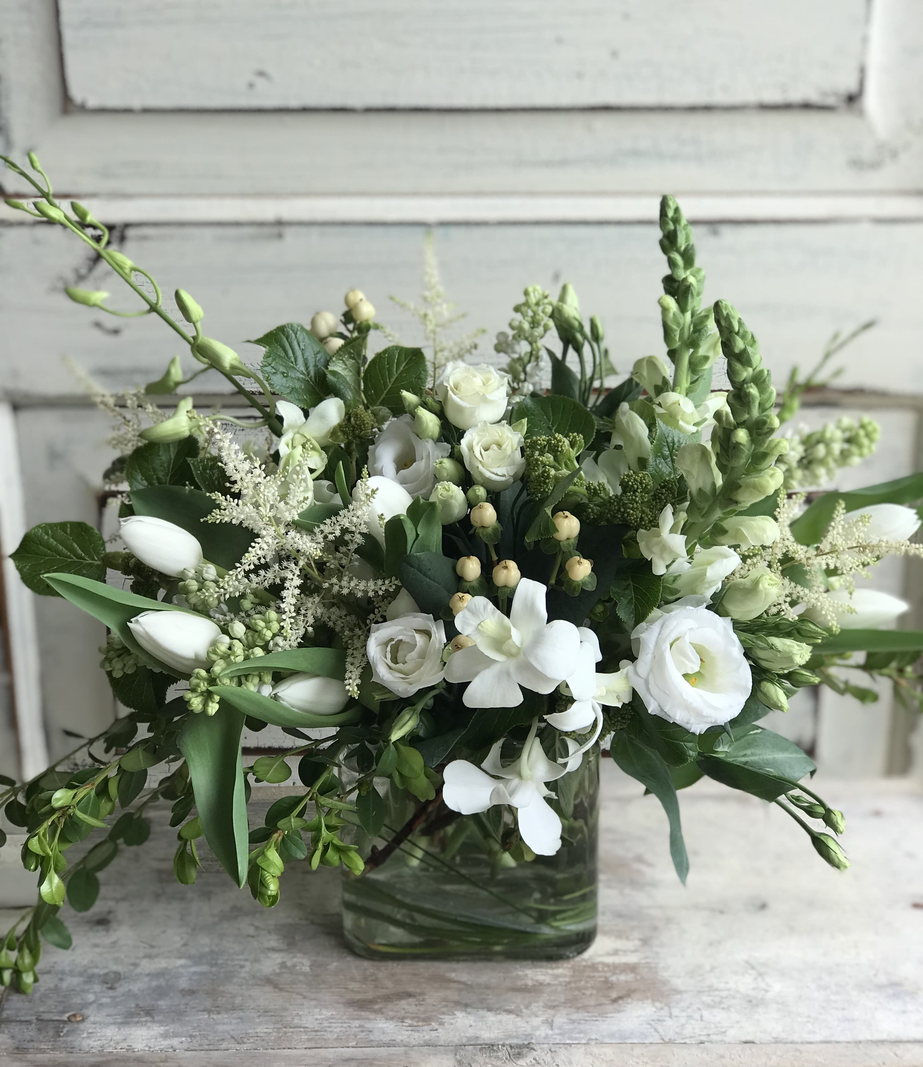 All White Low - A mix of seasonal blooms in all white and unique foliage arranged in a glass cube or bowl. Flower varieties will vary based on the time of year and our cooler inventory.