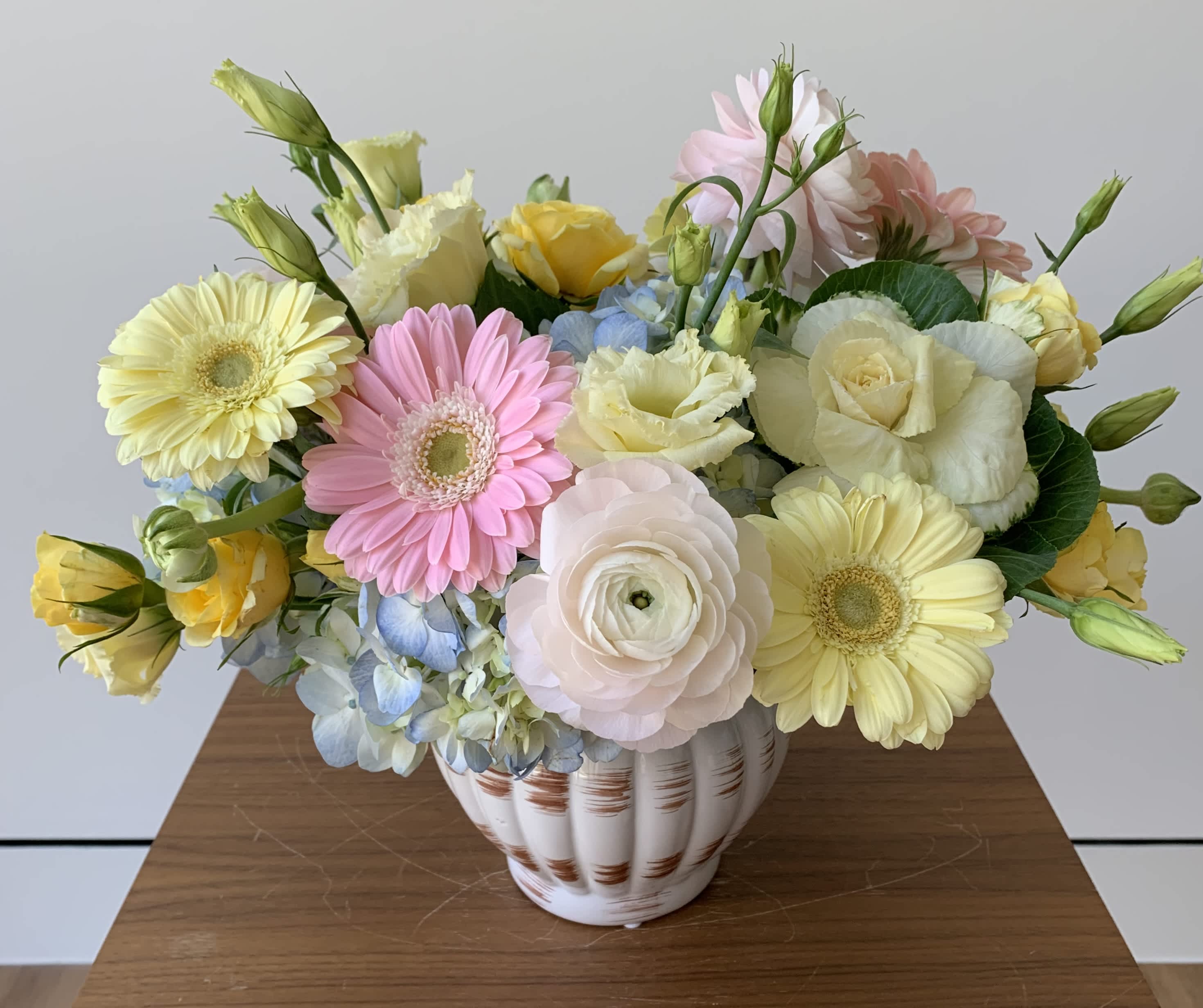 Delicate - A pastel flower arrangement in a ceramic white vase with premium flowers such as hydrangeas, roses, gerbers, ranunculus, and lisianthus. I mix creamy yellows, light pinks, whites and light blues to make a lovely flower centerpiece for any occasion you celebrate or commemorate.