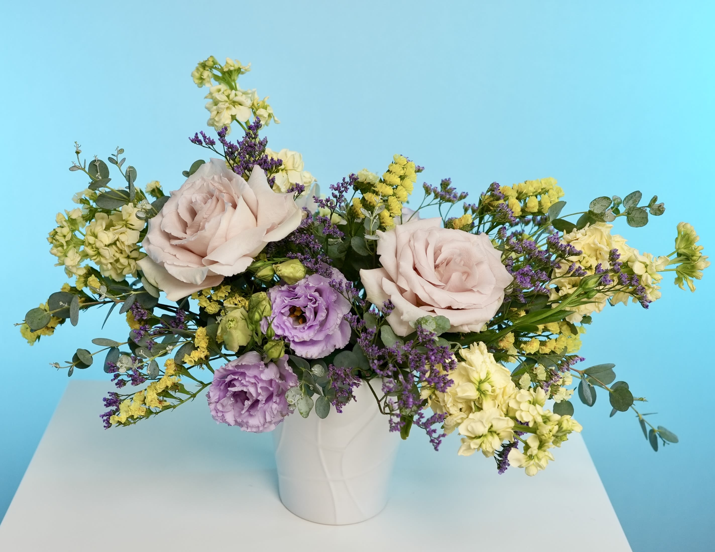 Whispering Meadow - Let tranquility bloom with Whispering Meadow — a soft, romantic arrangement inspired by the quiet charm of sun-drenched countryside fields. This bouquet blends blush garden roses, delicate lavender lisianthus, buttery yellow stock, and fragrant eucalyptus for a look that’s both graceful and grounded.  Perfect for thank-you gifts, peaceful celebrations, or elevating everyday moments, Whispering Meadow whispers elegance without saying a word. Its gentle scent of fresh florals and wild herbs creates a serene atmosphere wherever it’s placed. 