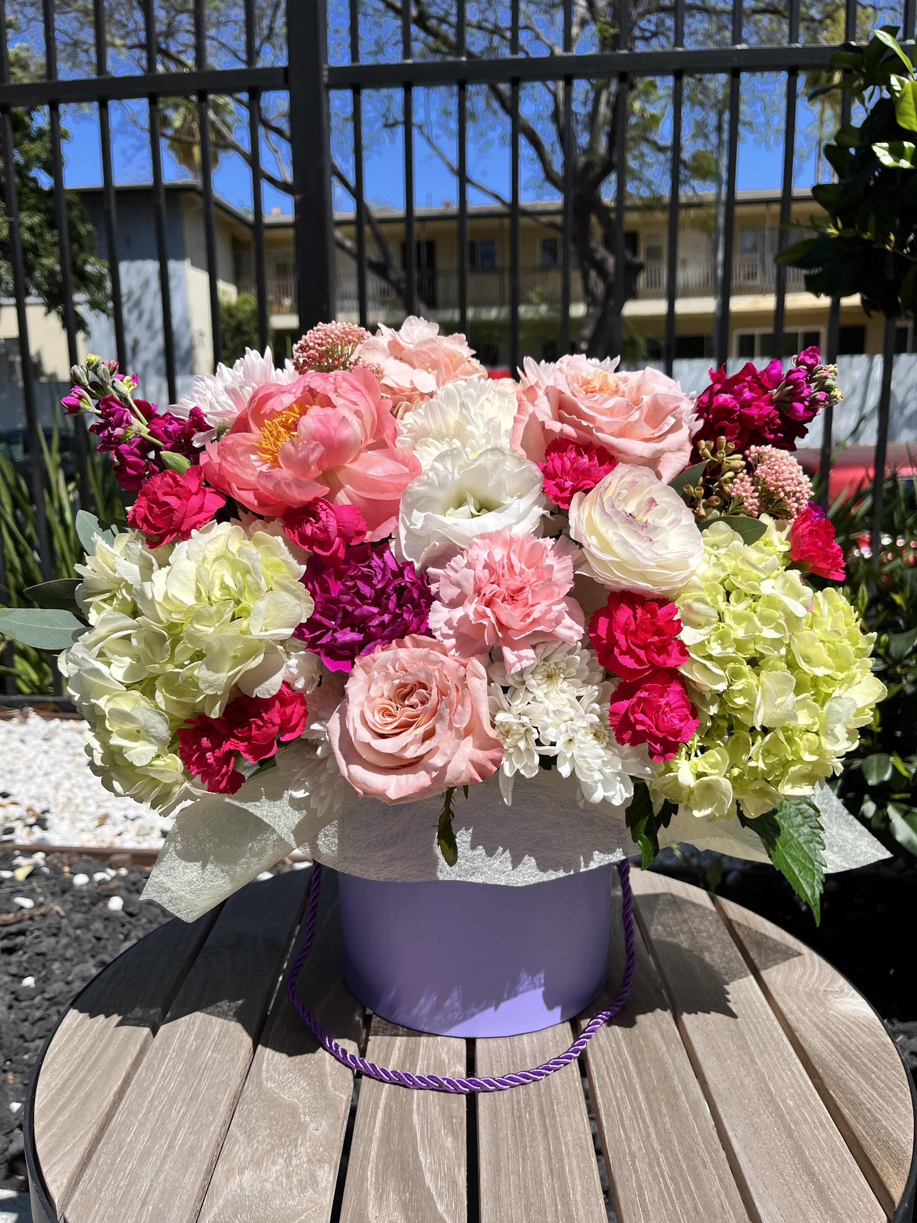 Summer Éclat Summer Éclat - Bursting with vivid color and refined textures, Summer Éclat is a joyful ode to bright days and elegant celebrations. This showstopping arrangement features garden roses in soft blush, hot pink carnations, fluffy white and green hydrangeas, blooming peonies, lisianthus, and cheerful chrysanthemums — all designed in a chic lavender hatbox for a modern, elevated finish. Ideal for birthdays, thank-you gifts, or unforgettable moments that deserve a dazzling floral touch. Style: Bold, luxurious, joyful Fragrance: Fresh garden florals with soft rose undertones