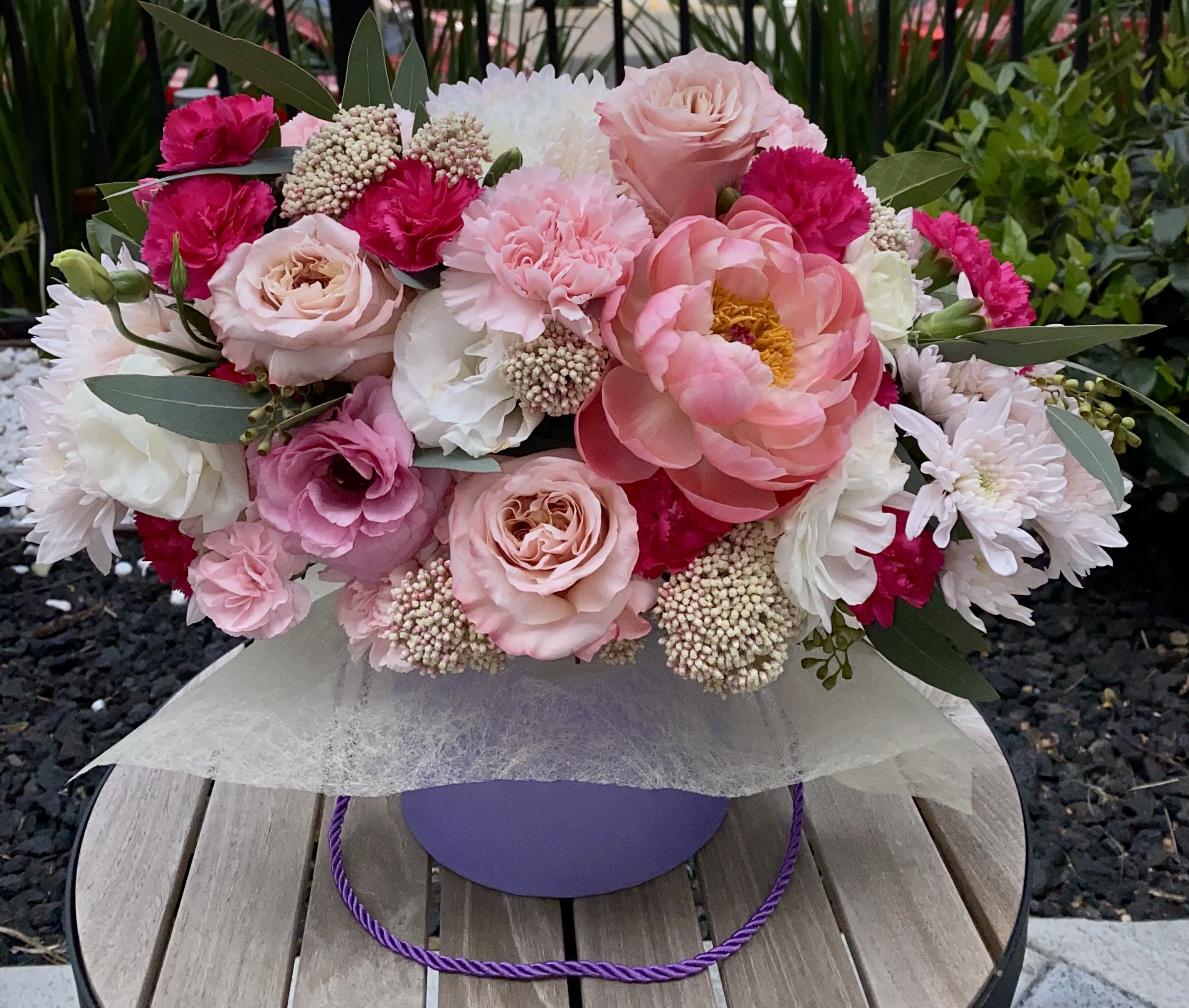 Rosé Luxe - Lush, romantic, and utterly captivating, Rosé Luxe is an opulent hatbox arrangement that embodies the elegance of a modern floral romance. Featuring soft blush roses, vibrant raspberry carnations, blooming peonies, lisianthus, chrysanthemums, and textured accents of yarrow and eucalyptus, this floral piece is as rich in texture as it is in charm.  Designed in a designer lavender hatbox, Rosé Luxe is the perfect gift for anniversaries, heartfelt celebrations, or when only the most exquisite will do.  Style: Romantic, bold, refined Fragrance: Soft rose and peony notes