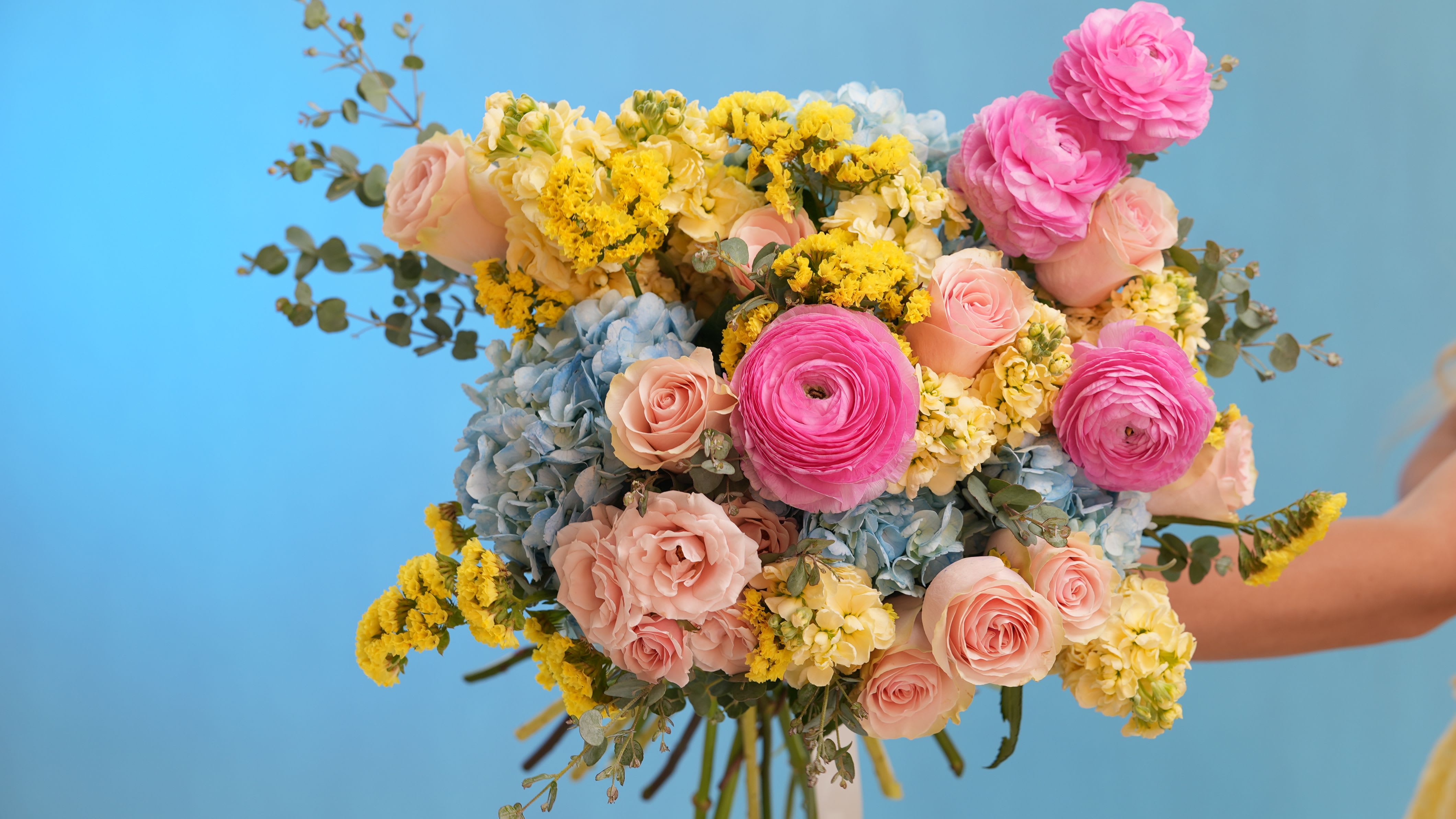 Katy’s Dream - Katy’s Dream – Signature Bouquet Step into a fairytale with Katy’s Dream, a breathtaking floral arrangement inspired by soft romance, golden light, and effortless charm. This handcrafted bouquet features a dreamy blend of blush roses, vibrant pink ranunculus, delicate yellow stock, sky-blue hydrangeas, golden solidago, and airy eucalyptus sprigs — all tied together with an elegant satin ribbon.  Whether you're celebrating love, beauty, or a special moment, Katy’s Dream brings timeless elegance to any occasion.  Style: Romantic, whimsical, joyful Fragrance: Lightly floral with fresh spring notes Perfect for: Birthdays, bridal showers, “just because” moments