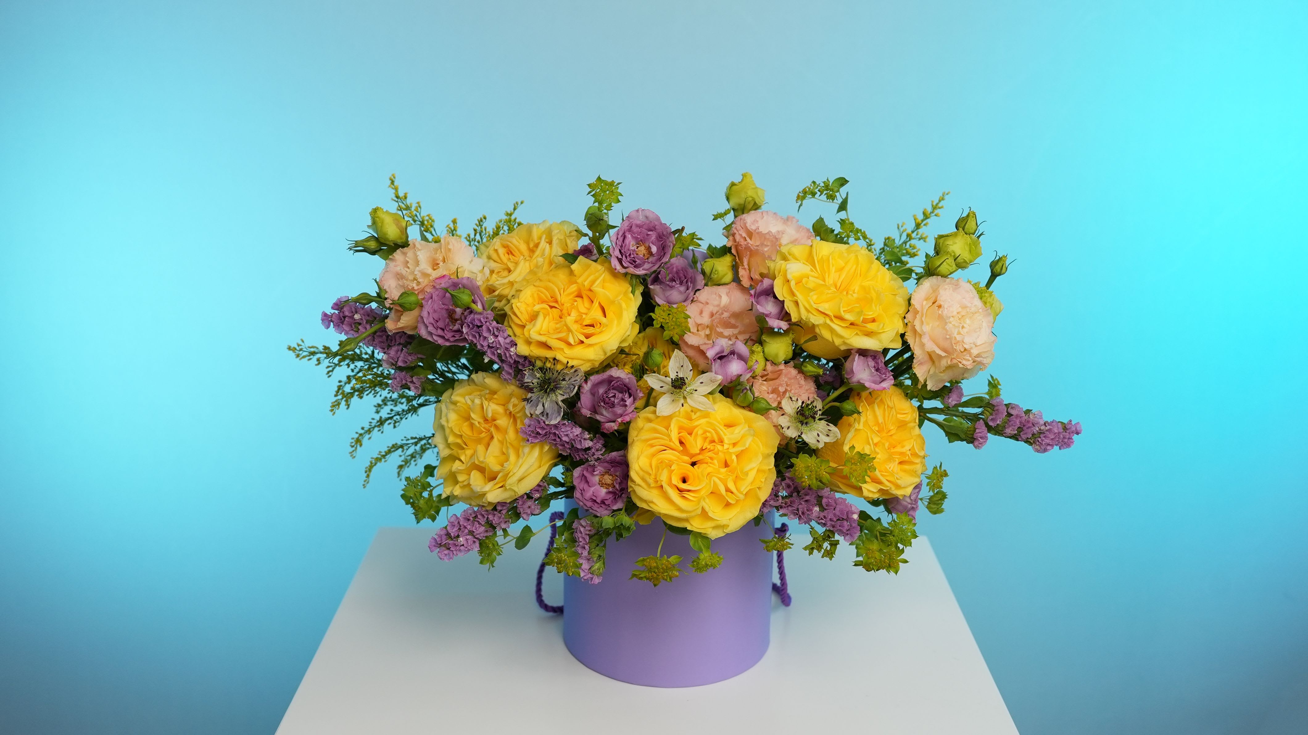 Château Fleur - Step into the charm of a French countryside estate with Château Fleur. This opulent arrangement features lavish golden garden roses, delicate lavender lisianthus, and airy pastel blooms woven with natural greenery. Presented in our signature lilac hat box, this bouquet embodies refined luxury and joyful romance — ideal for unforgettable celebrations or simply elevating the everyday.