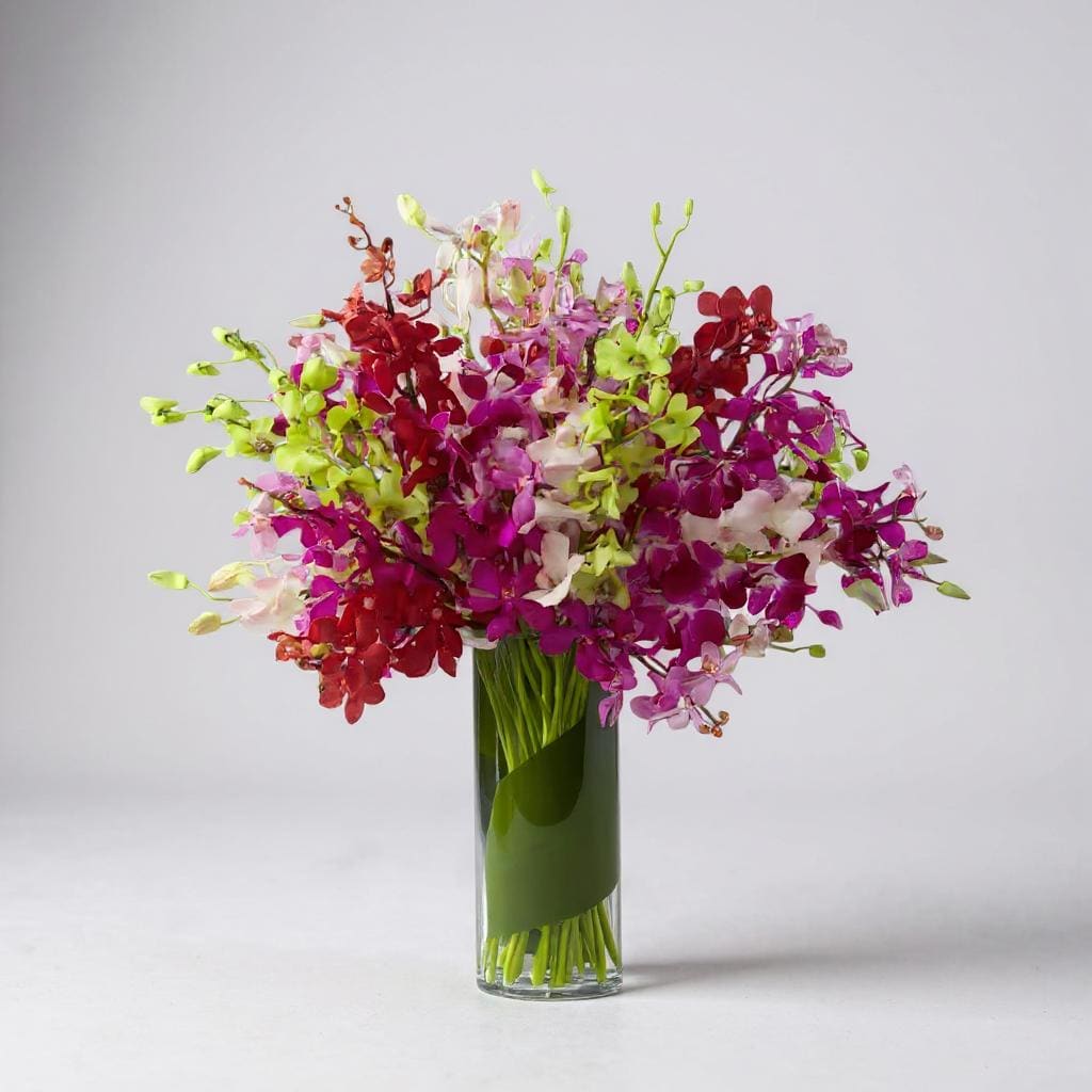 Luminous Luxury Orchid Bouquet - Let your sweet sentiments shine with vibrant color and exuberant elegance. An assortment of brilliant Dendrobium Orchids in the shades of red, lavender, green, fuchsia, hot pink, and pale pink are brought together to create a simply fantastic display. Wrapped in a single tropical leaf and perfectly arranged in a superior clear glass vase, this bouquet will delight your special recipient with its exquisite beauty and long-lasting blooms. Exact color of orchids may vary slightly.