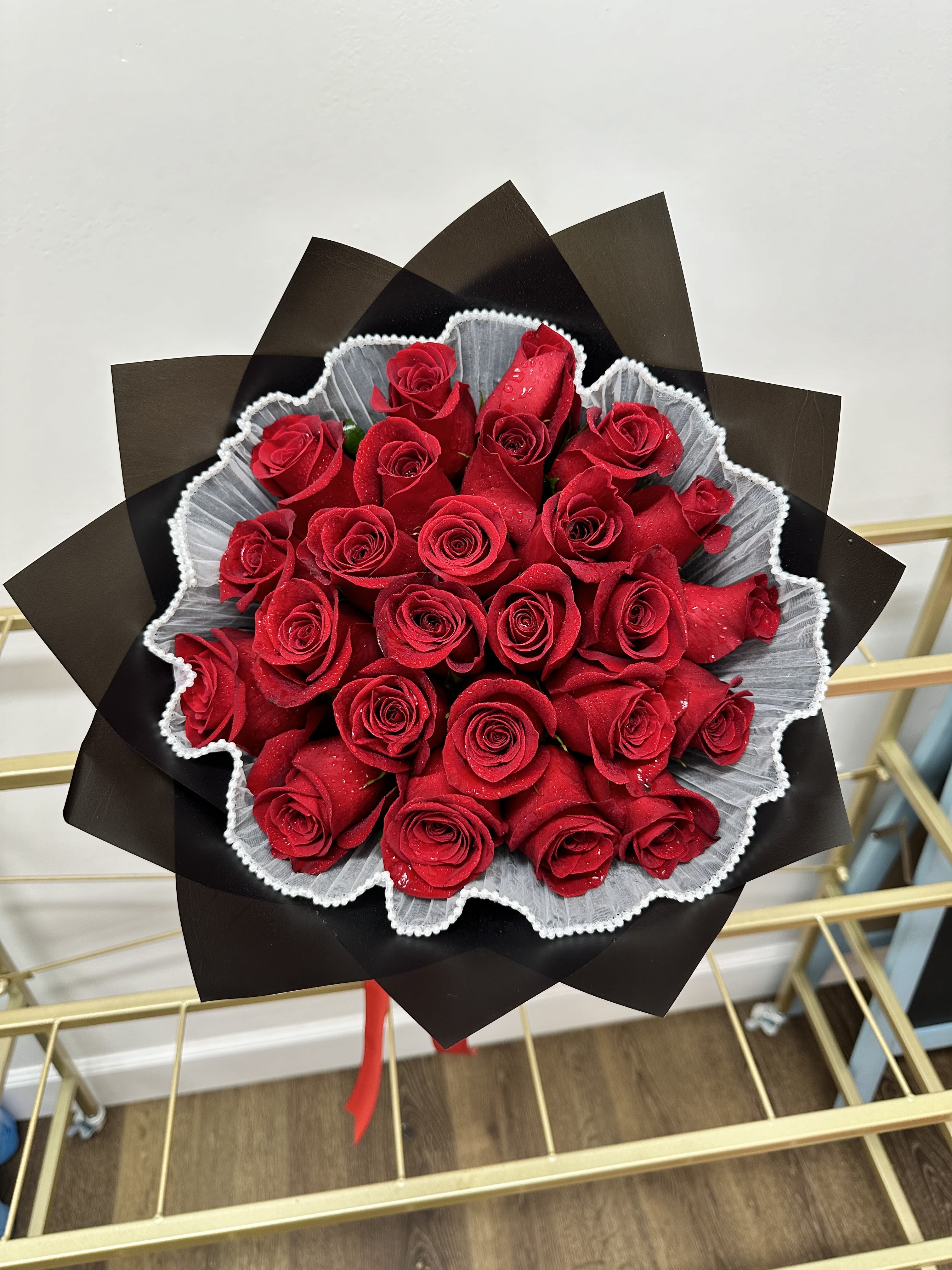 Crimson Elegance - This striking arrangement features vibrant red roses, beautifully wrapped in sophisticated black paper, with delicate white mesh adding a touch of contrast and elegance between the roses and the paper. Perfect for expressing love, admiration, or making any occasion special, this bouquet exudes passion and style. Please note, a vase is not included, giving you the freedom to display these stunning blooms in your preferred vase. 