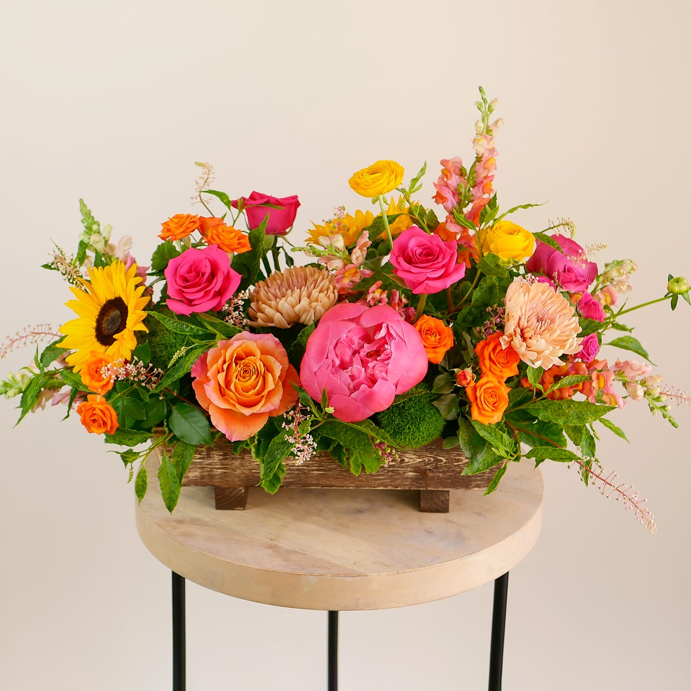 Can't Be Tamed - Bold, bright, and full of energy — &quot;Can’t Be Tamed&quot; is made for making a statement. This vibrant centerpiece features hot pink and orange roses, coral peonies, yellow ranunculus, sunflowers, snapdragons, and other mixed blooms, all arranged in a rustic wooden planter. It’s colorful, playful, and impossible to ignore! Arrangement approximately measures 30&quot; long and 18&quot; tall with flowers.