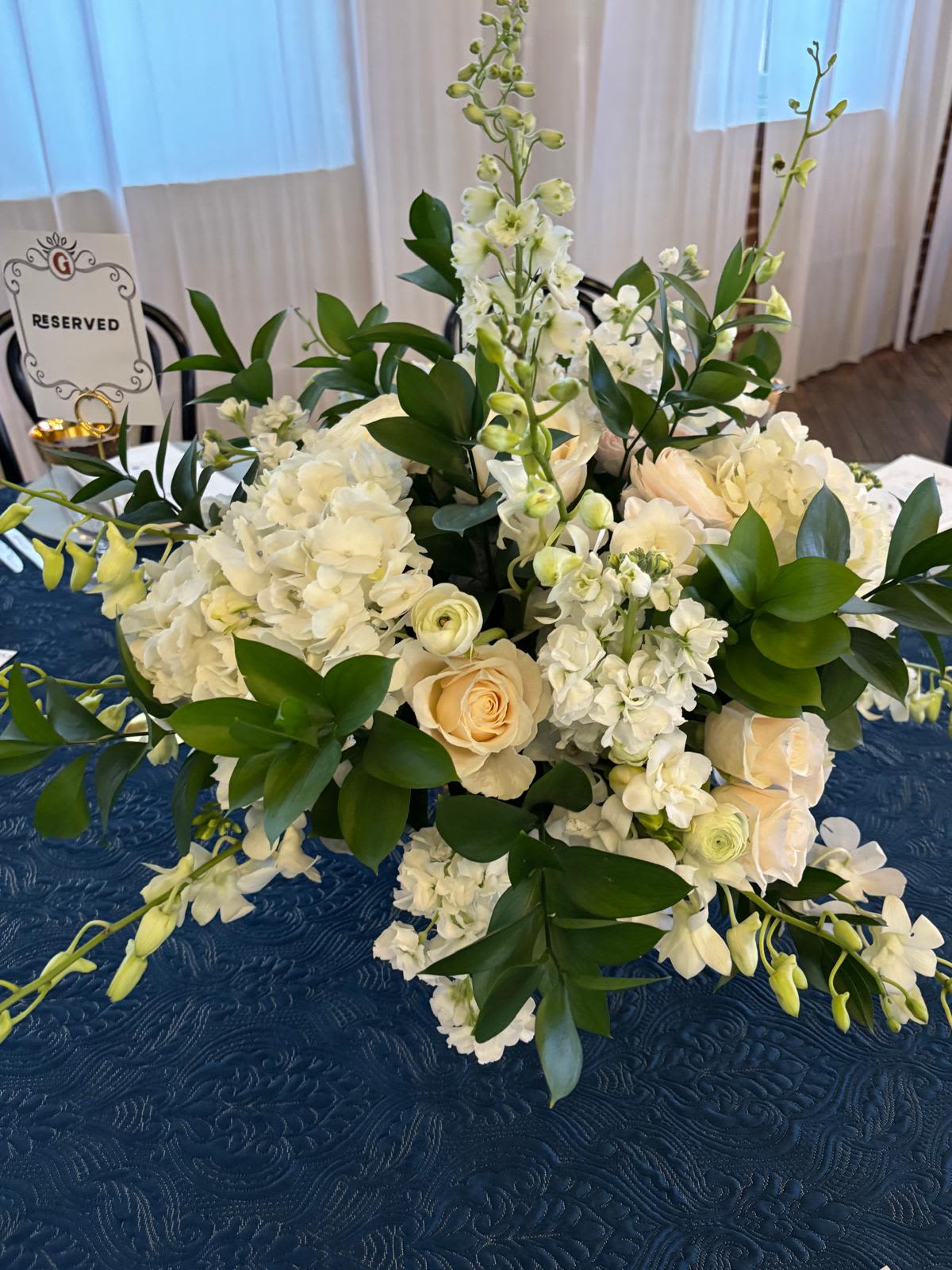 Ivory Elegance Ivory Elegance - A breathtaking all-white arrangement featuring creamy roses, lush hydrangeas, delicate lisianthus, and cascading orchids, elegantly framed with rich greenery. Graceful and timeless, this stunning centerpiece exudes refined sophistication — perfect for weddings, formal dinners, or luxurious event settings