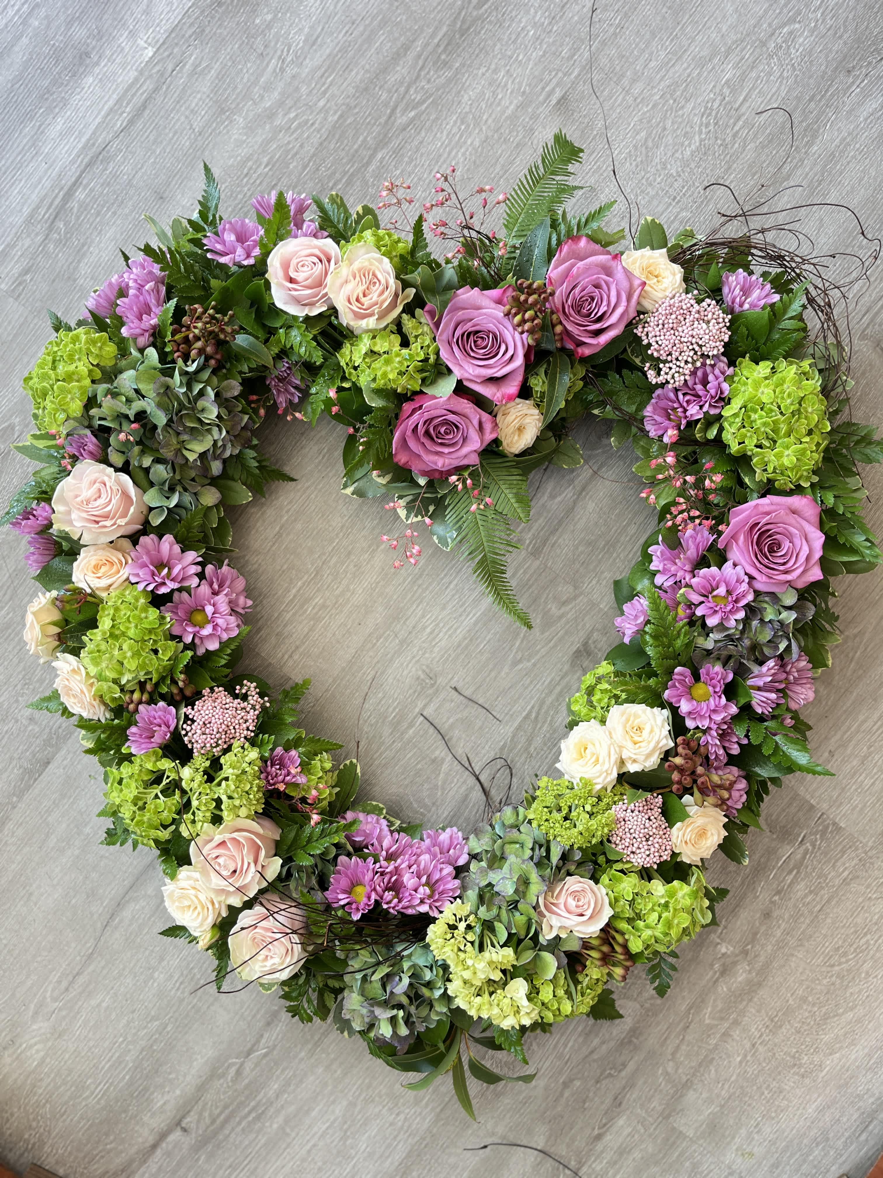 Cottage Garden Memorial Heart  - This gorgeous memorial wreath is a stunning way to send your expression of sympathy.  We use some of our favorite seasonal blooms such as roses, hydrangea and garden roses to create this beautiful design enhanced with a delicate hoop of angel vine twigs.  This design is elevated on an easel at the funeral home. This piece is not appropriate to send to a residence given its size and weight.  *other colors available - please call us or leave a note with your requests.  Measures Approx. 30&quot; across. 