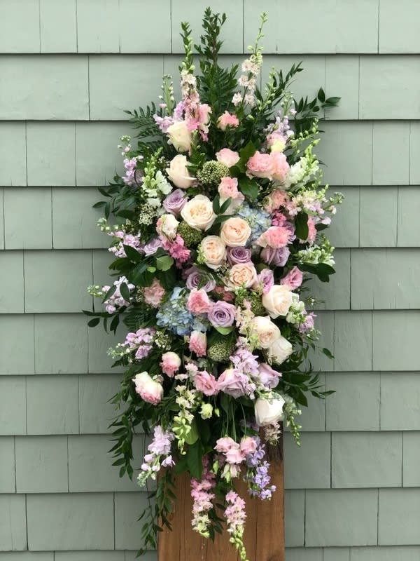 Pastel Traditions Spray - A pastel color palette creates comfort and grace with this Traditions Spray. Featuring a selection of muted blossoms such as blush pink, lavender and ivory with spring greens. A beautiful way to remember a loved one.    Other color combinations available.  Please contact us for consultation and availability.