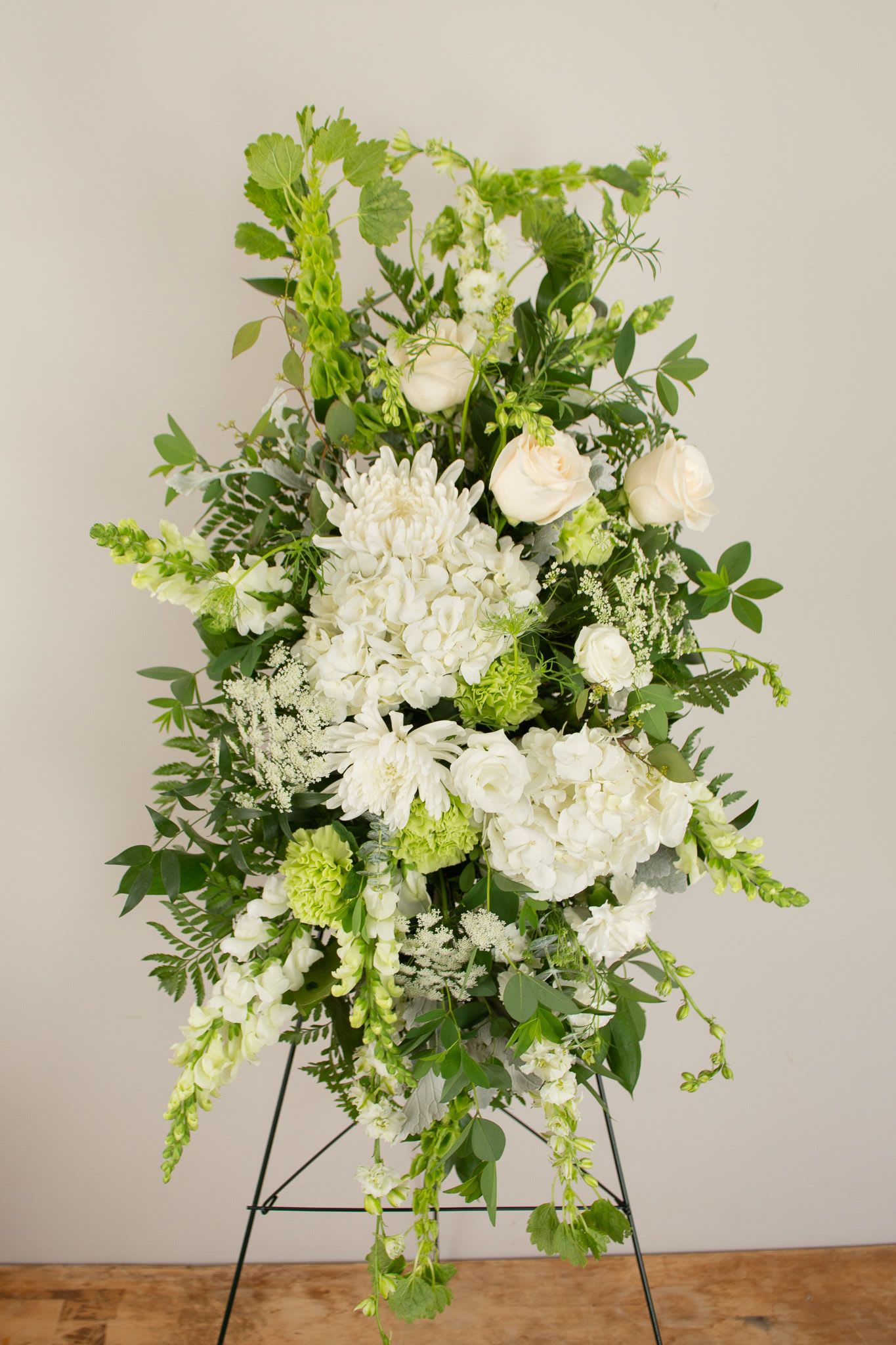 White Traditions Spray - A timeless expression of peace and remembrance, this standing spray features a graceful mix of seasonal white blooms, thoughtfully accented with fresh greenery. It is presented on a stand and serves as a beautiful tribute to honor and celebrate a loved one’s life.