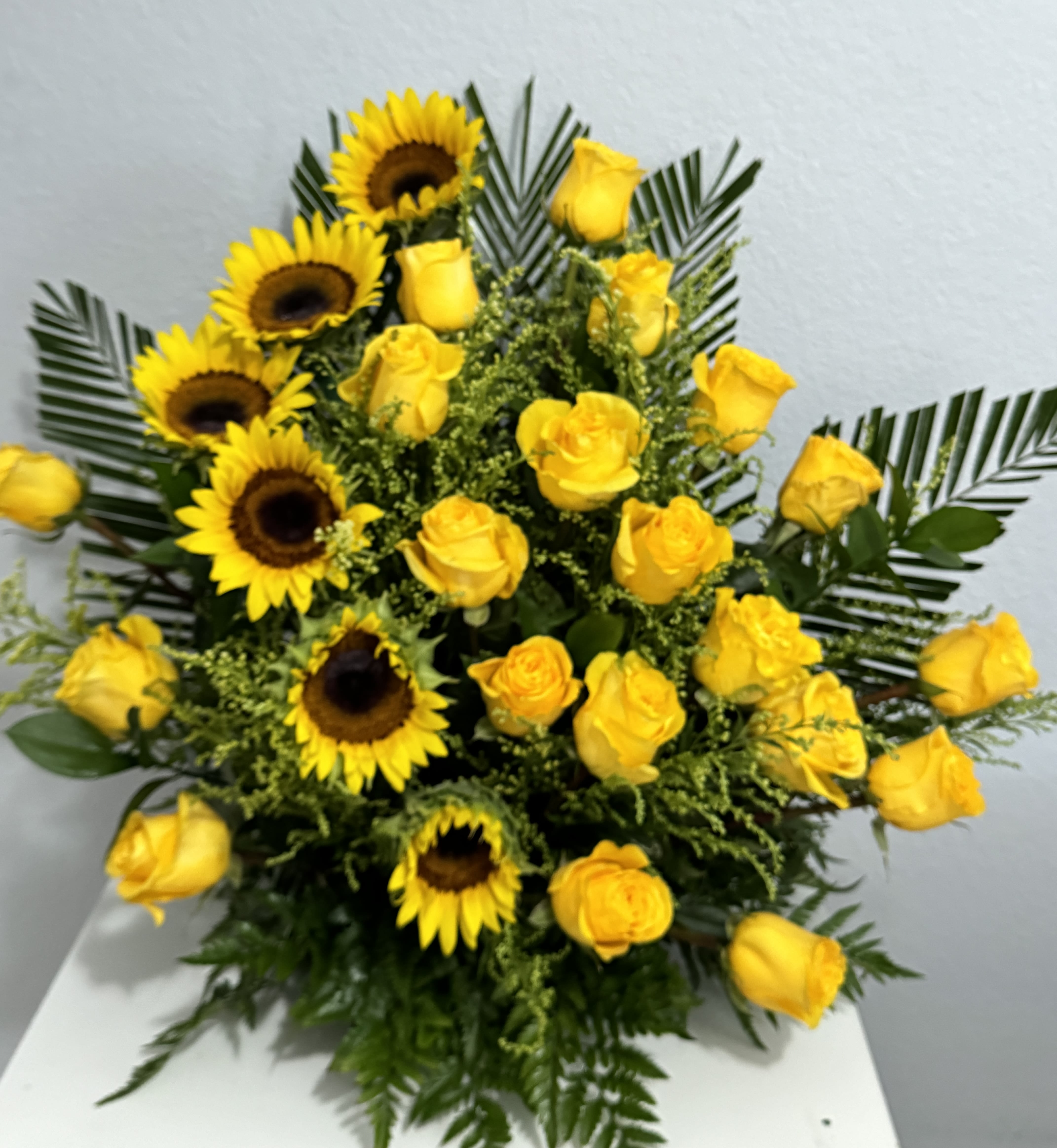 Light of Heaven - A radiant altar arrangement featuring 20 golden yellow roses, 6 bright sunflowers, lush greenery, and delicate solidago. Designed to bring warmth, peace, and light to any sacred space or memorial tribute.