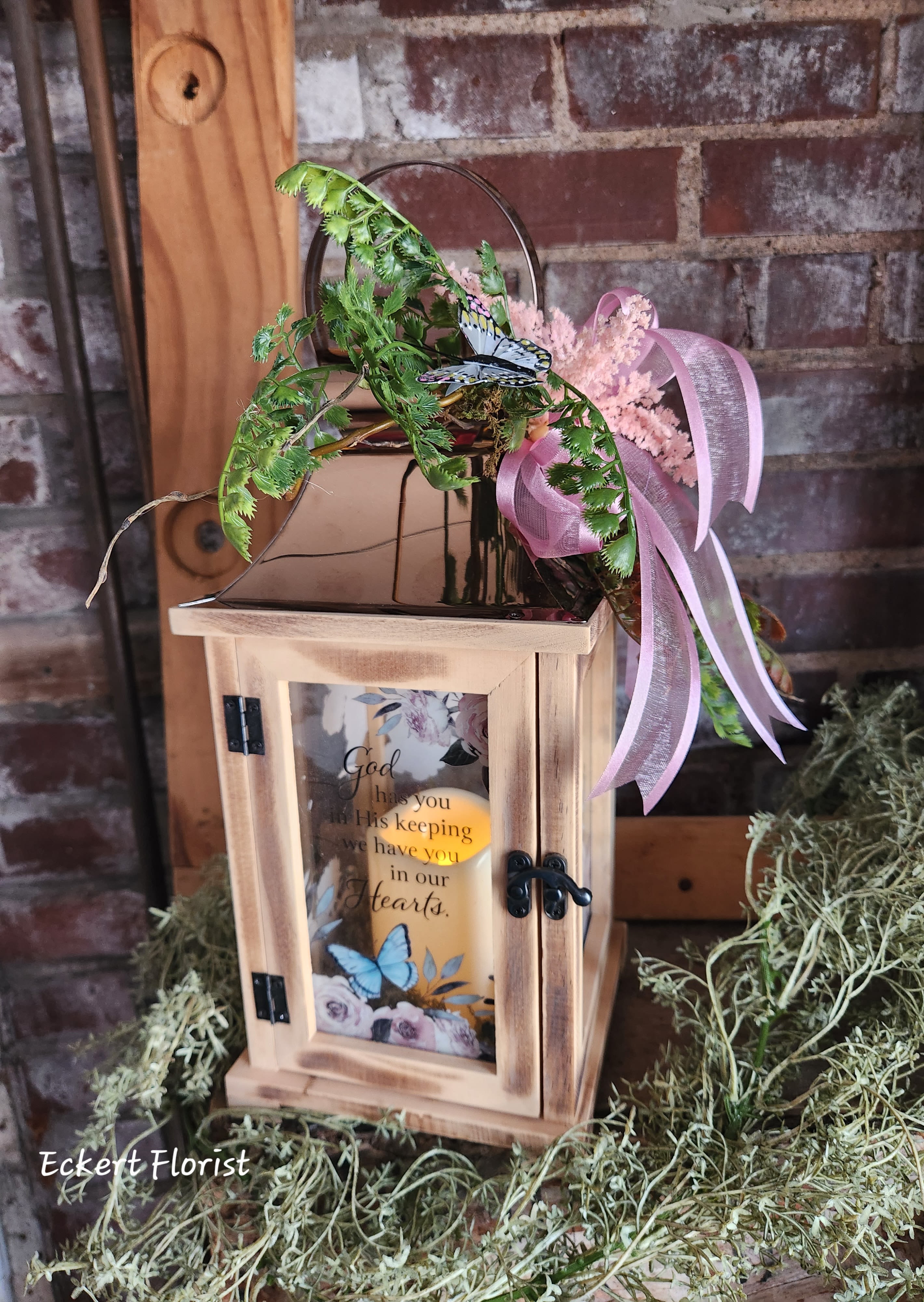 Eckert Florist's &quot;God Has You In His Keeping&quot; Lantern *Our Local Delvery Only - This lantern is made from quality wood and a stainless steel copper finish top. It features a built-in automatic timer which runs for 6 hours on and 18 hours off (batteries included) and is uv printed with a sentimental quote: &quot;God has you in His keeping, we have you in our Hearts&quot; Suitable for hanging or free-standing use inside. W: 6.25&quot; H: 13.5&quot; D: 6.25&quot; *Our Local Delivery Only