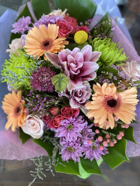 Dreamer Bouquet Dreamer Bouquet - A vibrant and cheerful bouquet bursting with color and texture. Soft peach gerberas and blush roses are paired with lilac chrysanthemums, and lime green spider mums. Accents pink hypericum berries and delicate filler flowers add playful charm, all nestled in lush greenery and wrapped in soft lavender and pink tones for a fresh, joyful presentation.