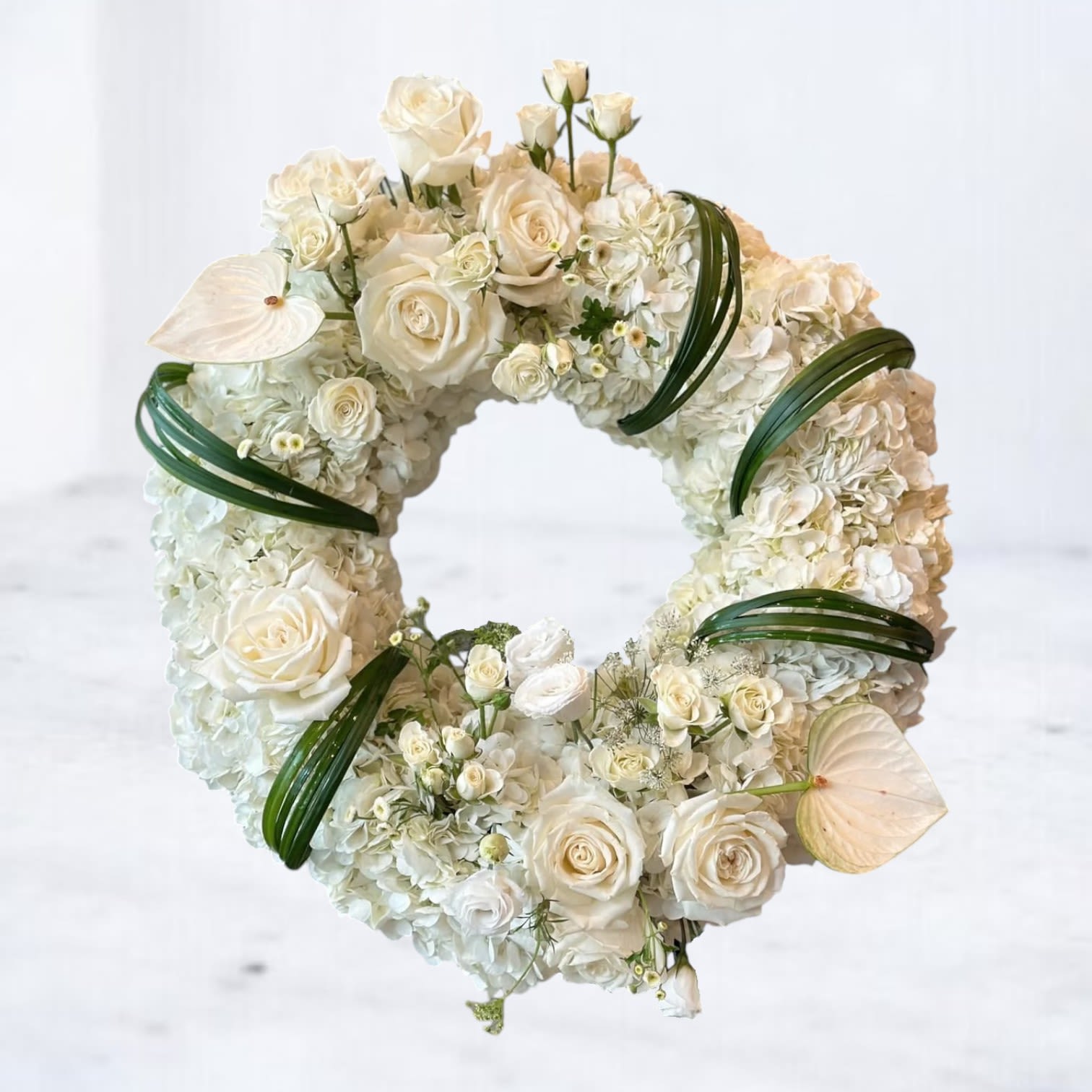 Serenity Circle Wreath - Honor a loved one's legacy with the Serenity Circle Wreath, a timeless expression of remembrance and peace. Crafted with pure white roses, hydrangeas, and delicate accent flowers, this elegant funeral wreath is accented with soft greenery and graceful anthurium blooms for a modern touch. The circular design represents eternity and the enduring bond of love, making it a heartfelt tribute for funeral services, memorials, or to convey your deepest condolences. Let the Serenity Circle Wreath convey your sympathy with elegance and grace.  Easels are included in the price of all wreath arrangements to ensure easy display at services. 
