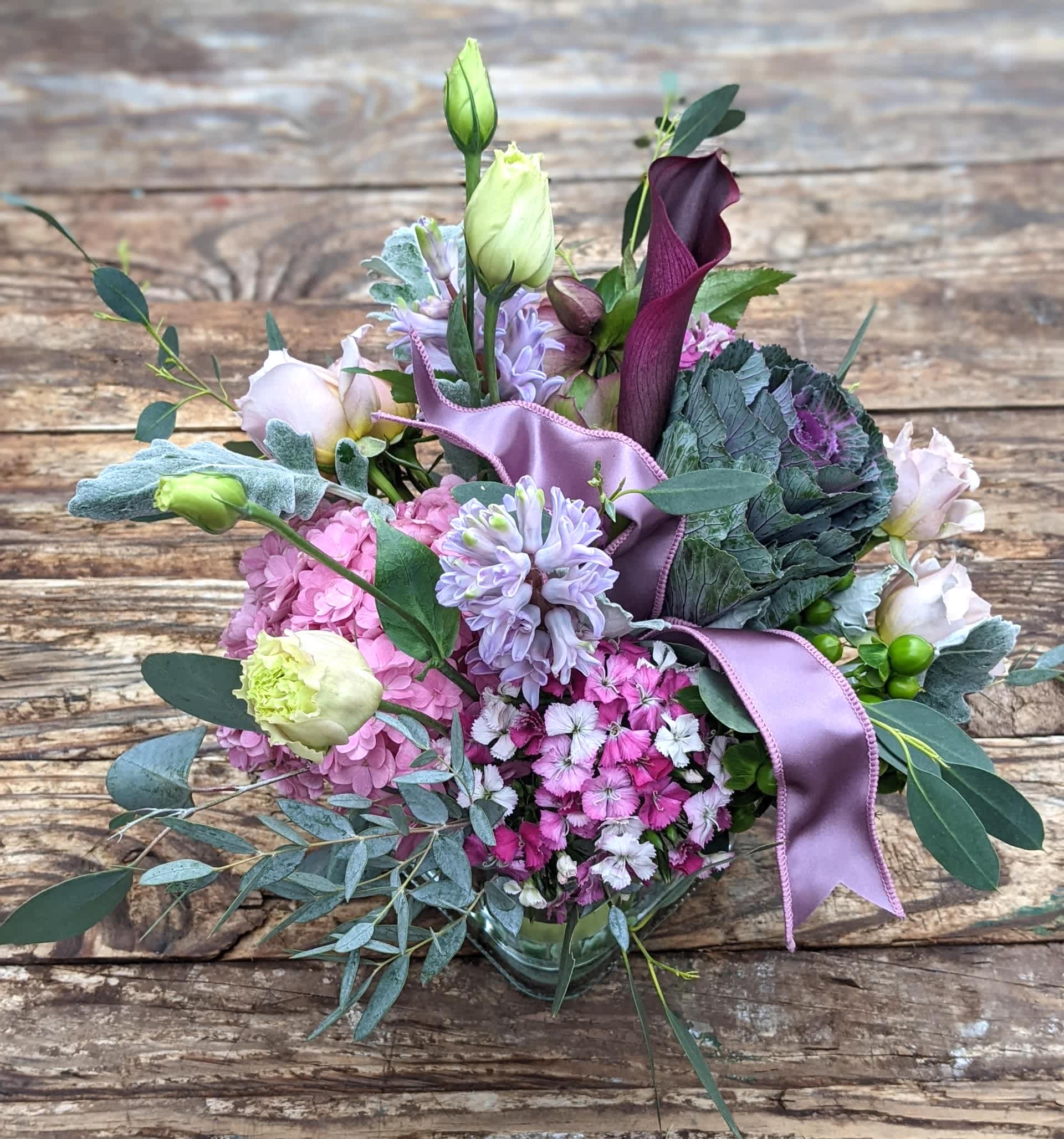 Hugs and Kisses - Soft arrangement featuring shades of lavender and pink accented with assorted foliage. Presented in a clear glass container with exposed stems.