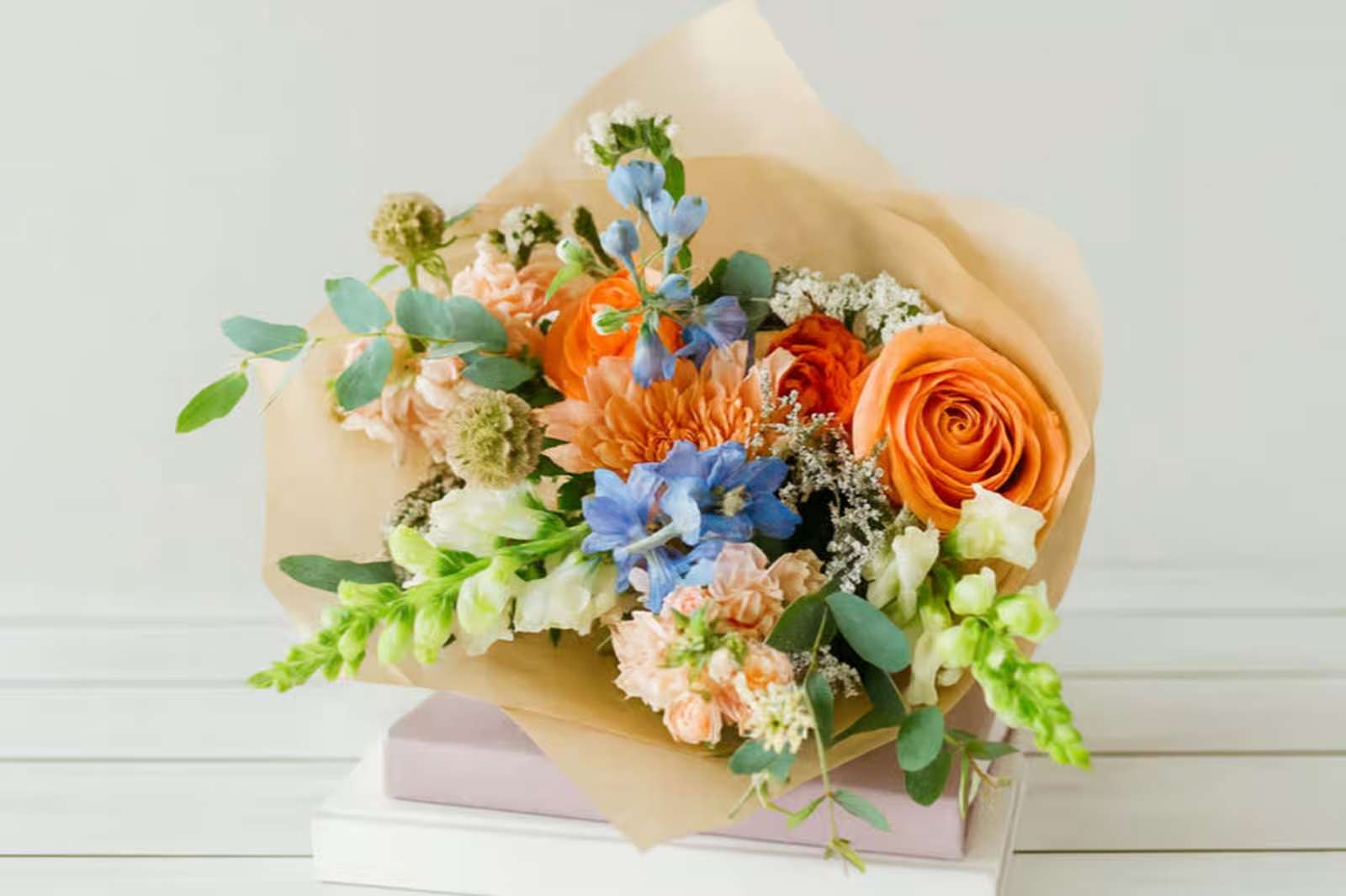 Primavera - Introducing Primavera – the perfect way to bring a touch of spring into your home! This beautiful wrapped bouquet is full of life and vivid colors, guaranteed to fill your special someone with joy. The cheerful mix of orange roses, white snap dragons, light blue delphinium and peach stock makes Primavera a feast for the eyes. It’s sure to bring sunshine into any room and make even the most somber winter day feel like springtime. Whether you’re looking for the ideal gift for friends, family or yourself, Primavera is sure to put a smile on anyone’s face. Get in the spring spirit with Primavera and let us help spread some sunshine today!
