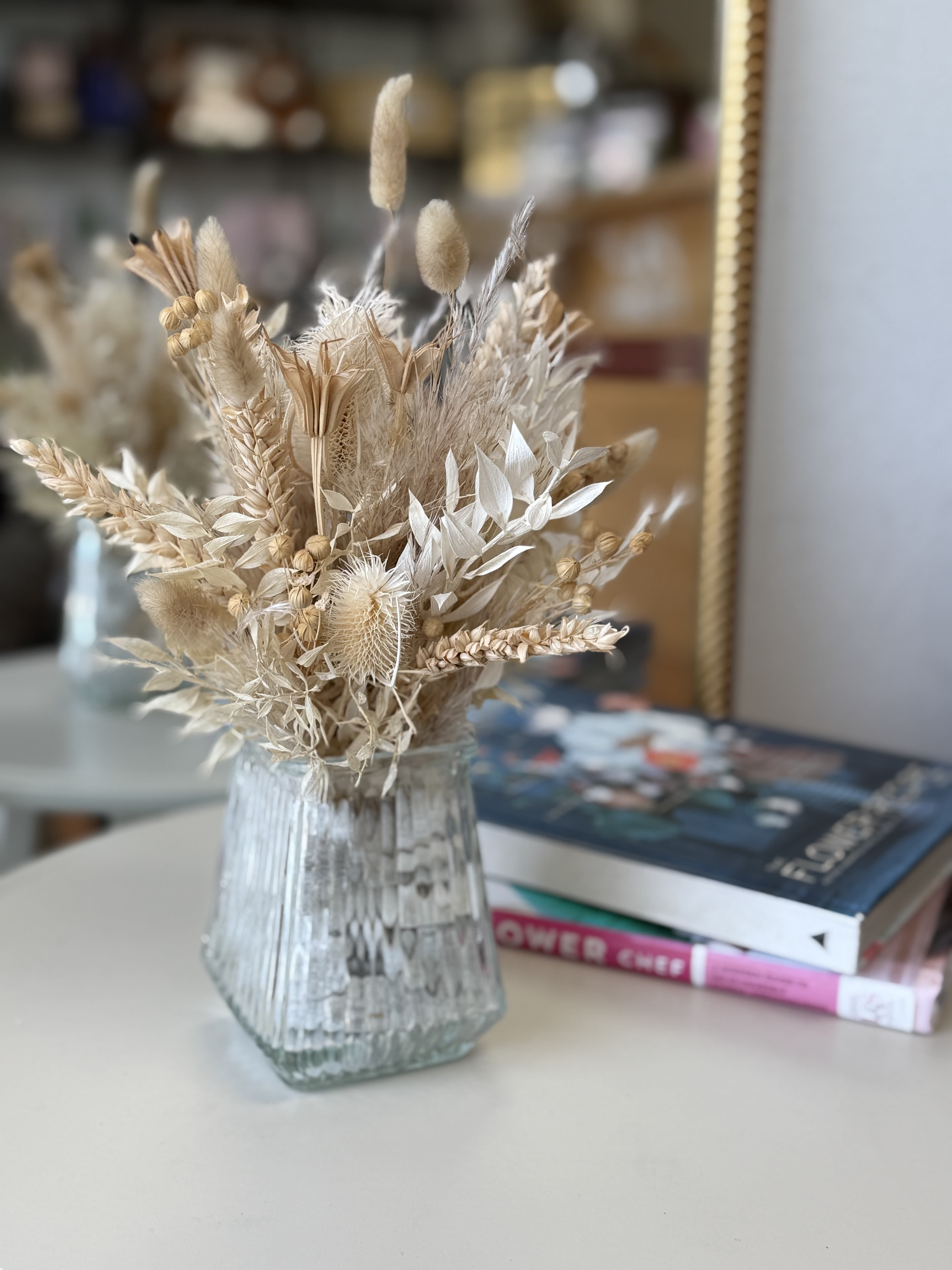 Dried Accent Arrangement #1 - Modern and minimal, this neutral-toned arrangement blends creams, soft beige, and sand-colored preserved flowers with sculptural accents like palm spears and bunny tails. It’s a serene, artful display that brings calm and class to any setting. One of a kind – while we can craft something similar, no two arrangements will ever be identical. Each piece is made by hand with care, using only the highest quality preserved blooms.
