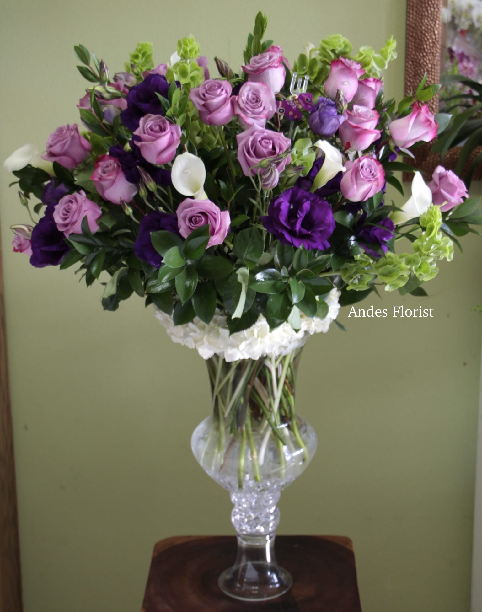 Sheena - Grand Lavender Roses, Purple Flowers Calla Lillies  - This was an arrangement we made for a customer, and we loved it so much we had to share with all of you! Our Sheena is displayed in our grand glass luxury vase with crystal accents. Two dozen lavender roses stand tall among Calla Lilies, Lisianthus, exotic greens over a bed of hydrangeas.   (We had this arrangement in our display case ready for our customer to pick up, and two others saw it and ordered the same grand design.... true story!)  *Remember: We can customize the color scheme to your desire. 
