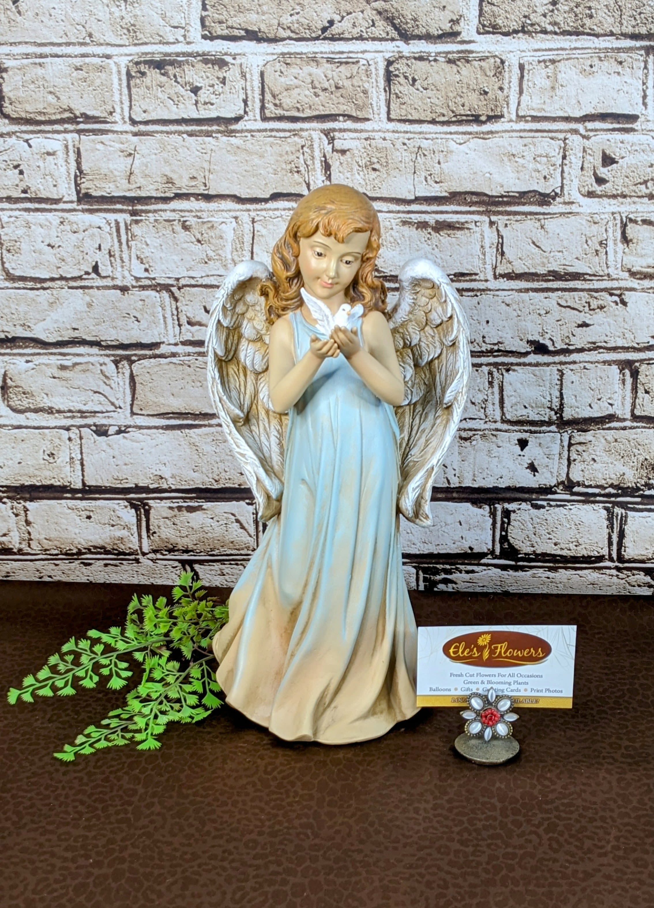 Serene Angel Serene Angel - This serene Angel radiates peace and grace, featuring flowing robes in a soft blue hue and beautifully detailed wings. She gently cradles a dove in her hands, symbolizing love, hope, and harmony. Perfect as a heartfelt sympathy gift or a meaningful decorative piece, this angel brings comfort and a sense of tranquility to any space. Made from a resin material. Indoor use only. Approximate Dimensions: 12"H x 6"W