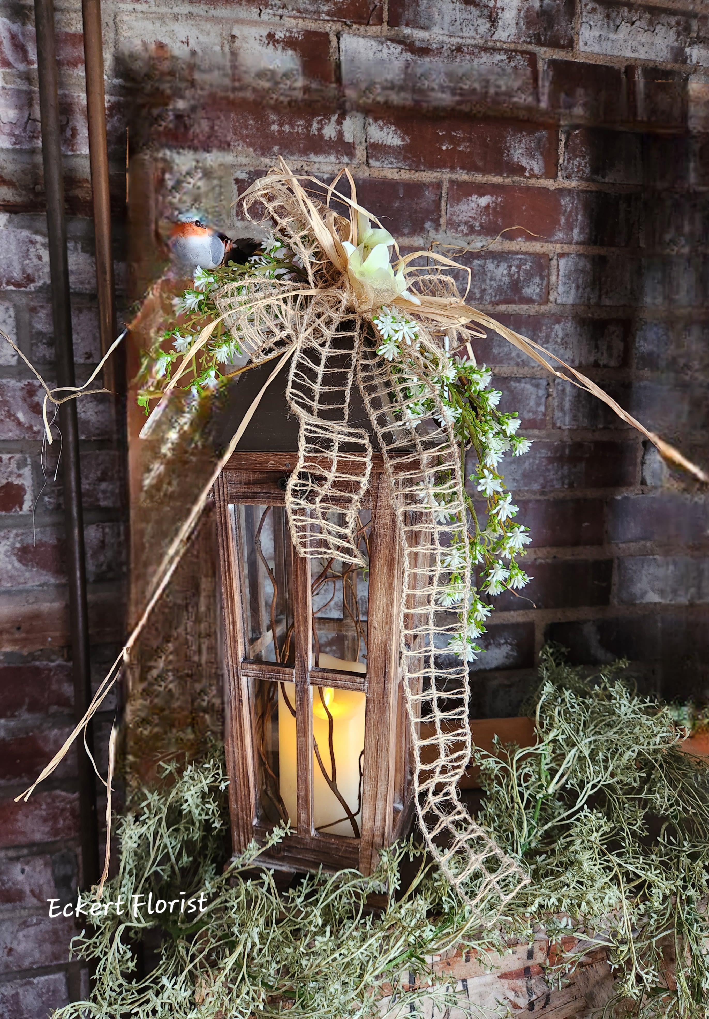 Eckert Florist's Brown Tapered Lantern *Our Local Delivery Only Eckert Florist's Brown Tapered Lantern *Our Local Delivery Only - Brown wooden with glass tapered lantern with brown tin roof measures approx. 20" High x 7" Wide. Included is a battery operated candle with our signature bird, floral decor and designer ribbon. Batteries included. *Our Local Delivery Only.