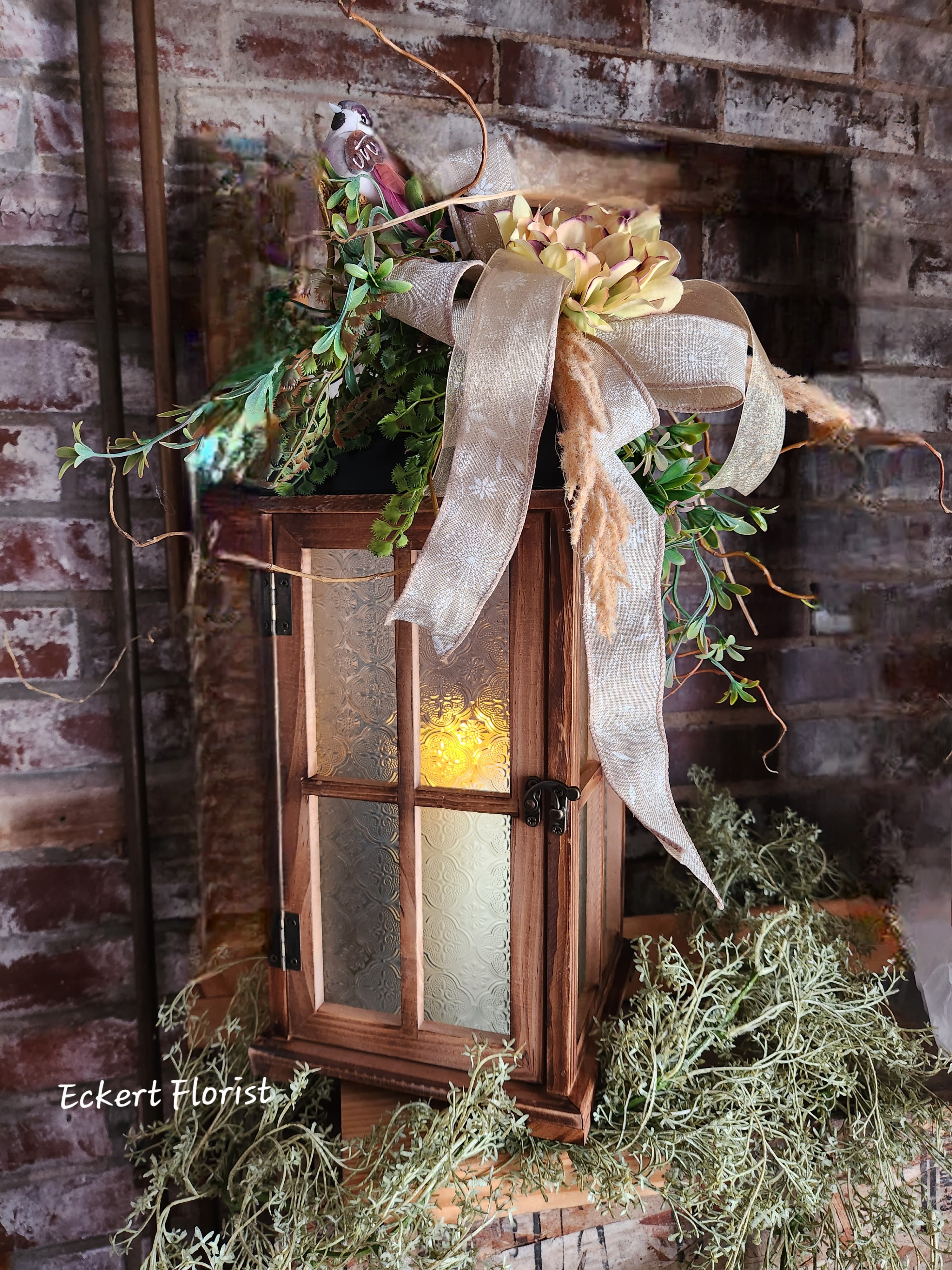 Eckert Florist's Medium Brown Textured Glass Lantern *Our Local Delivery Only Eckert Florist's Medium Brown Textured Glass Lantern *Our Local Delivery Only - This brown wooden lantern arrives with textured glass, battery operated candle, floral decor and designer ribbon. Our signature twigs and bird is also included. Lantern measures approx. 21" High x 8" Square. Batteries are included. *Our Local Delivery Only