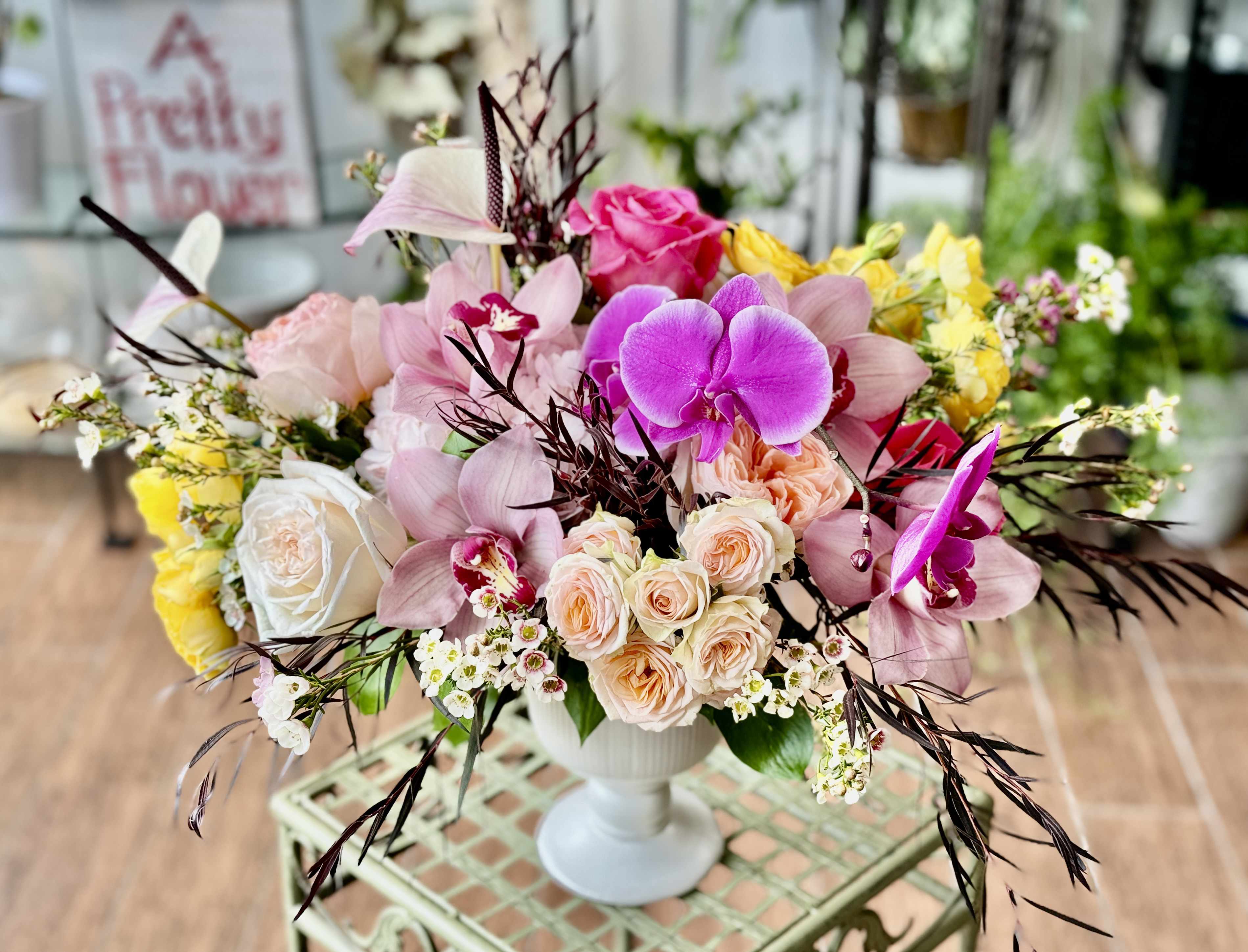 Lauren - Vibrant arrangement with a variety of textures and blooms, arranged in a ceramic pedestal vase. Available in this style or with deep tones aesthetic with a black vase. Let us know in special requests if you prefer a deep tones version in a black vase!