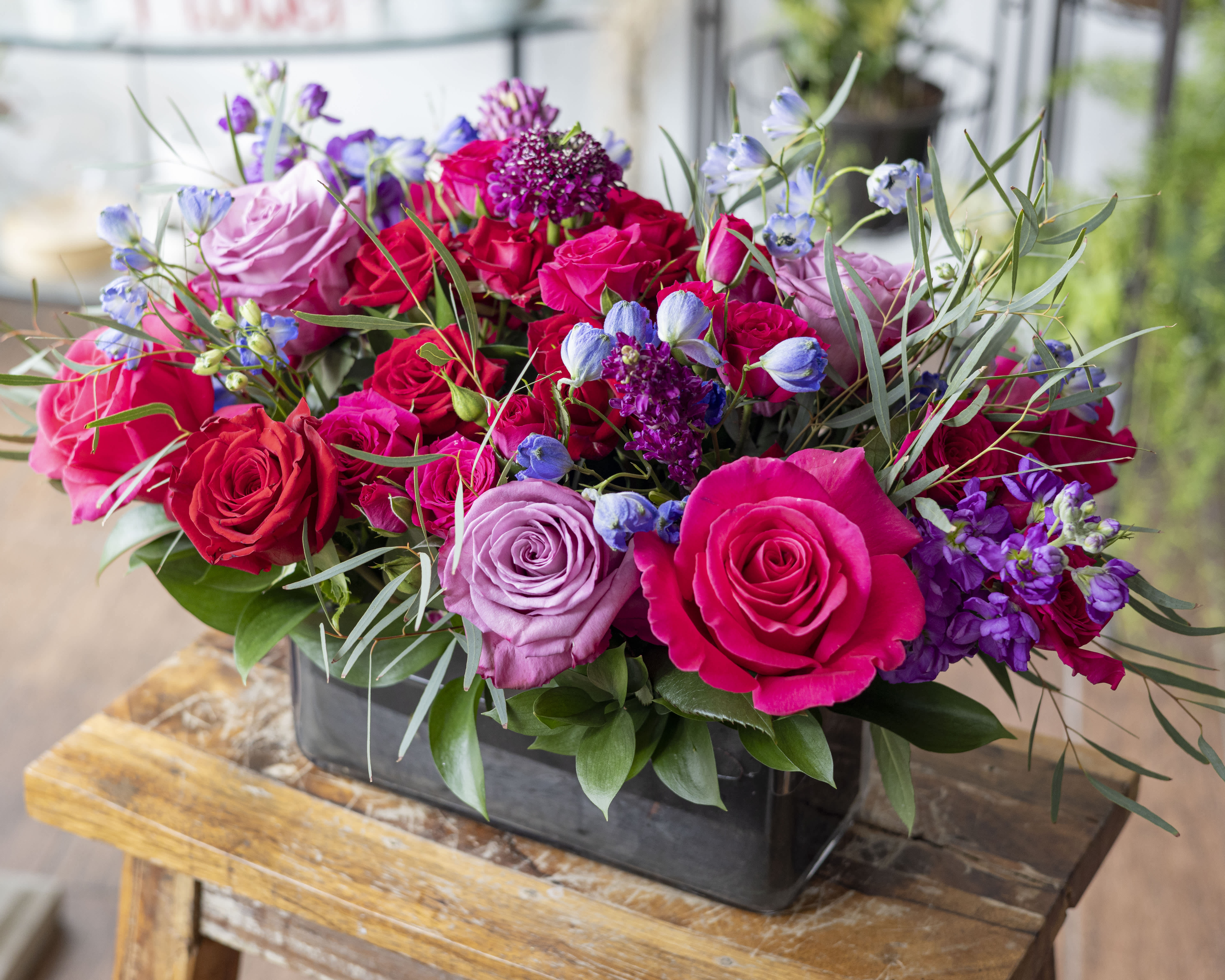 Judy - Vibrant colors in a variety of blooms arranged in a short design within a clear glass vase. 