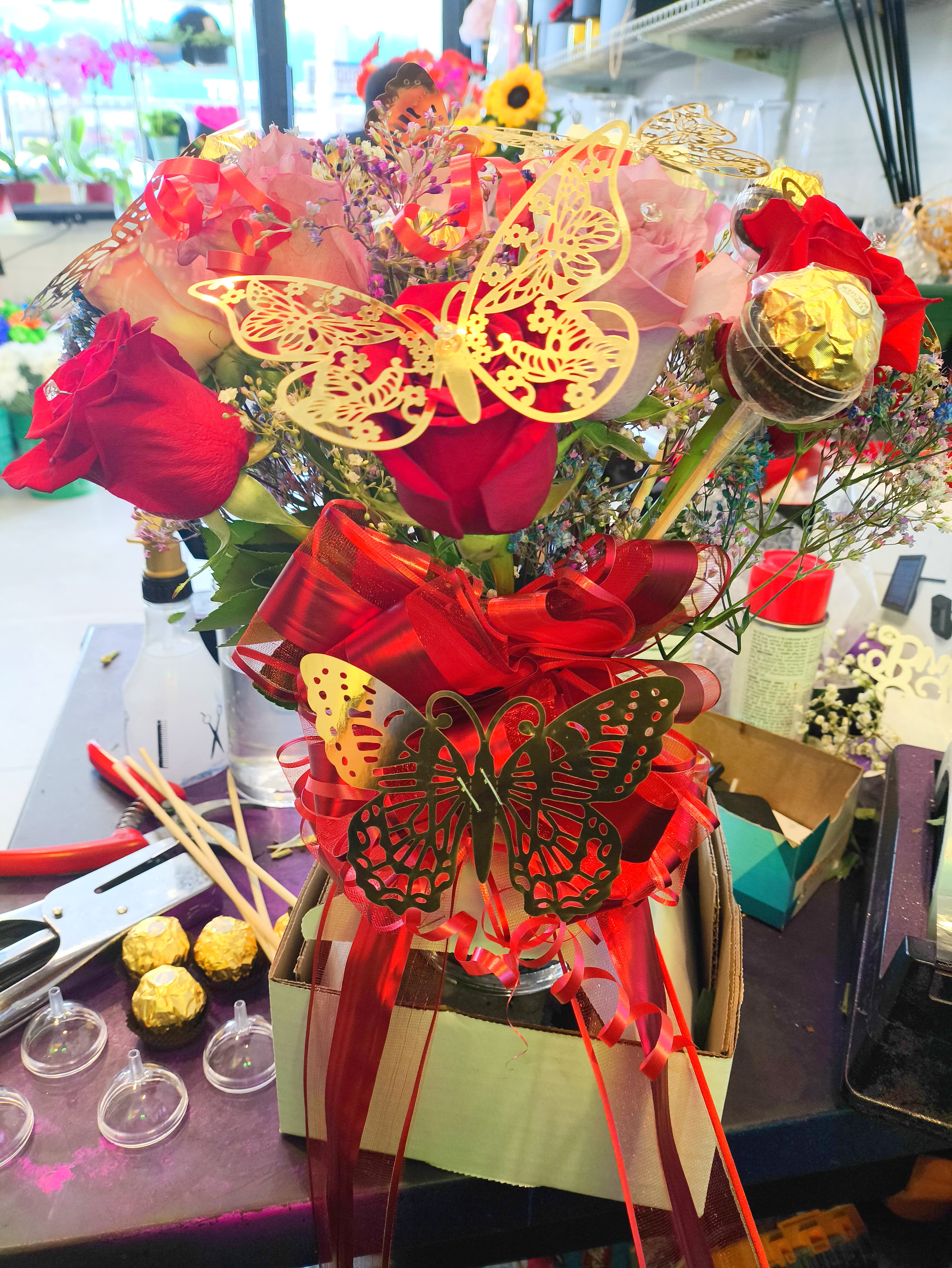 Pastel mixed Roses with diamonds and gold butterflies and chocolates - We design a dozen mixed roses in a vase with gold butterflies and chocolates and diamonds in the roses with a big red bow.