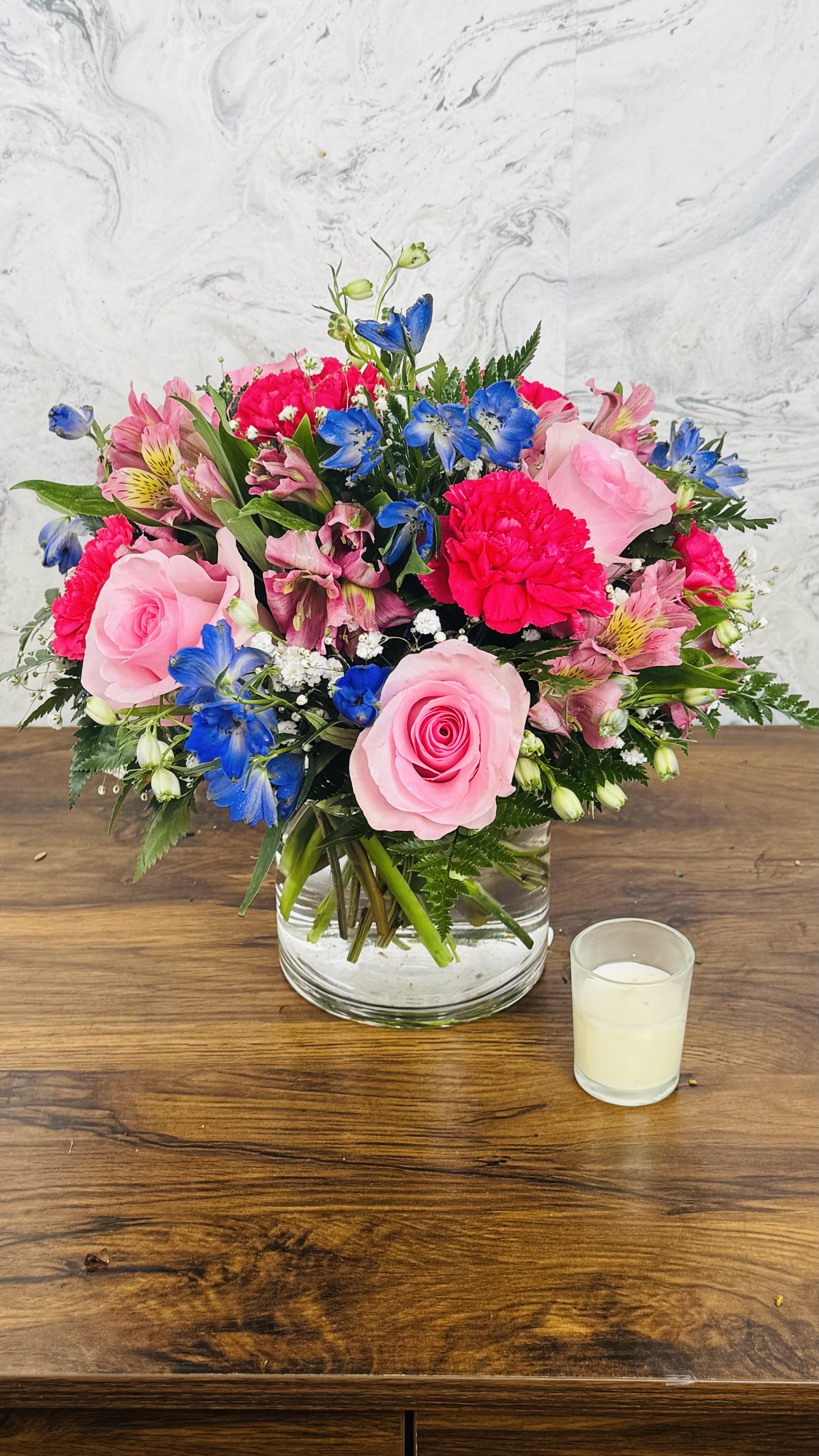 Blush &amp; Bloom - Blush &amp; Bloom features delicate pink alstroemeria paired with vibrant hot pink roses and carnations, complemented by elegant blue delphinium. This arrangement exudes a cheerful and romantic charm, perfect for celebrating special moments or adding a touch of elegance to any space. The combination of soft pinks and striking blues creates a visually stunning display that symbolizes affection, admiration, and joy.