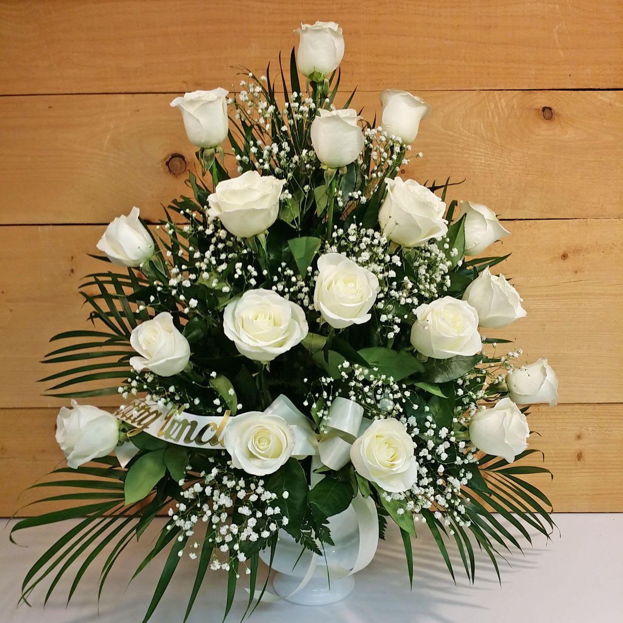 18 White Rose Sympathy Arrangement - The White Rose Sympathy Arrangement by Savilles Country Florist, consisting of 18 white long stem roses skillfully arranged in a white urn and accented with a white bow, green filler leaves and baby's breath.