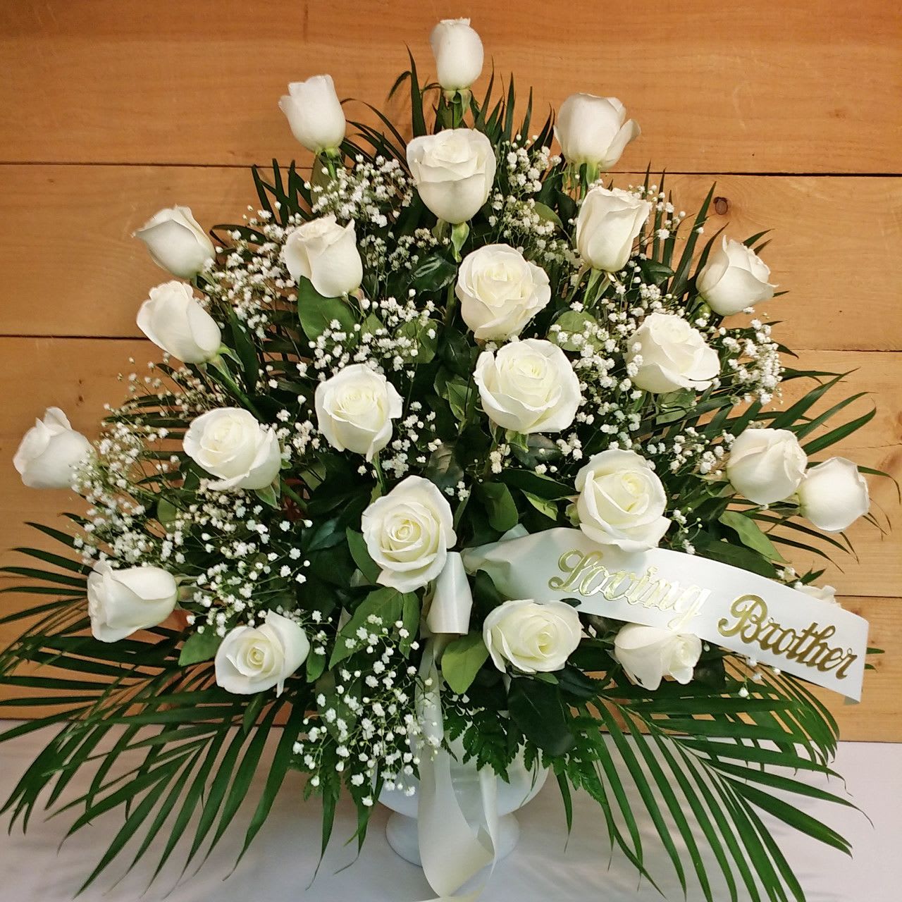 24 White Rose Sympathy Arrangement - The White Rose Sympathy Arrangement by Savilles Country Florist, consisting of 24 white long stem roses skillfully arranged in a white urn and accented with a white bow, green filler leaves and baby's breath.  