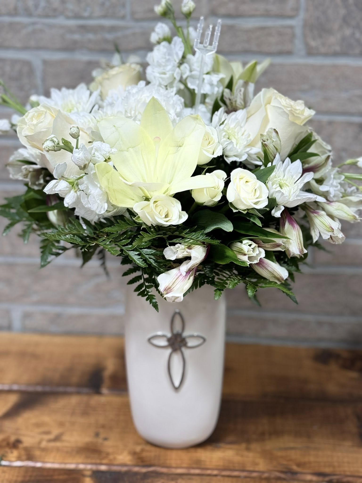 Divine Serenity Bouquet  - Gracefully arranged in a white ceramic vase adorned with a delicate cross, the Divine Serenity Bouquet is a heartfelt expression of peace, faith, and remembrance. Featuring a soothing blend of soft blooms in calming whites, this arrangement is perfect for honoring a loved one, offering comfort, or celebrating a special spiritual moment. Whether sent as a sympathy gesture or displayed in a place of worship, this bouquet carries a message of hope and gentle beauty.