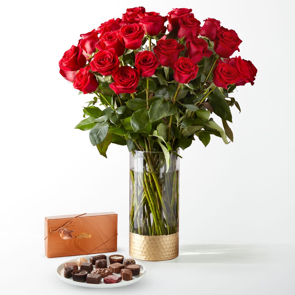Red Roses with Chocolate  - Make a grand romantic gesture with this luxurious gift set from Miami Flowers Design, the top florist in Miami, Florida. Featuring an opulent bouquet of long-stem red roses paired with a decadent box of premium assorted chocolates, this arrangement is the ultimate symbol of love, passion, and indulgence. The radiant red roses are beautifully displayed in an elegant glass vase with a hammered gold base, making this design as timeless as it is breathtaking.  Whether you're celebrating an anniversary, Valentine's Day, a birthday, or simply surprising someone special, this classic duo of flowers and chocolates is guaranteed to leave a lasting impression. Each rose is carefully hand-selected by our floral experts at Miami Flowers Design to ensure freshness, beauty, and elegance in every petal.  With same-day flower delivery in Miami, Coral Gables, and surrounding neighborhoods, we make it easy to send love straight to their door. Our commitment to quality and care has made us a favorite among customers looking for the best romantic flower arrangements in Miami.  Order now from Miami Flowers Design and elevate any occasion with the perfect combination of timeless red roses and delicious gourmet chocolates—crafted and delivered with love and style. 