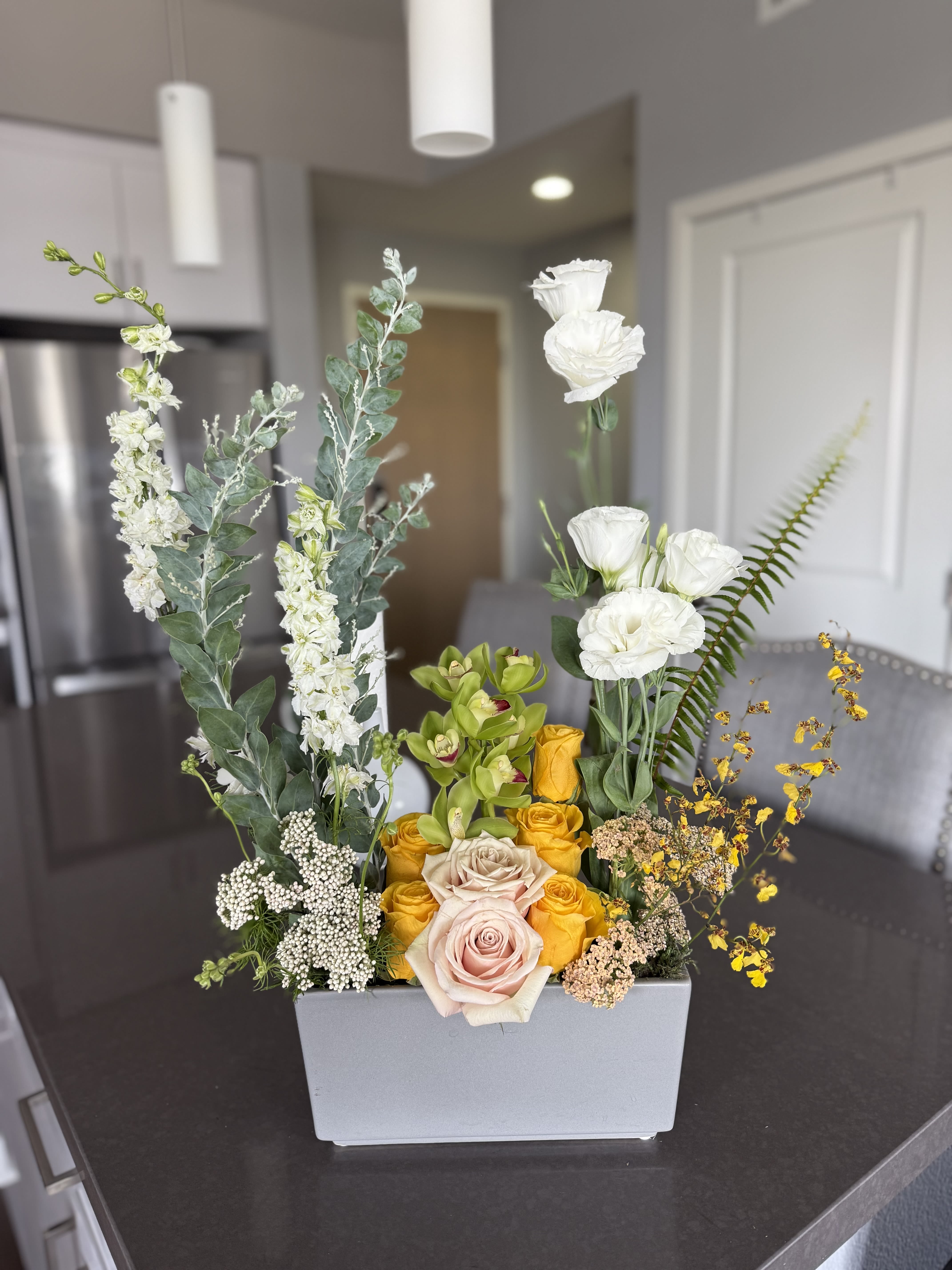 Golden sunrise modern Golden sunrise modern - Golden Sunrise Modern is a contemporary floral arrangement that radiates elegance and warmth. This sleek, rectangular design features vibrant golden-yellow roses, soft blush roses, fresh white lisianthus, exotic green cymbidium orchids, delicate oncidium orchids, and sculptural accents of eucalyptus, fern, and Queen Anne’s lace. The upright architectural shape creates a stunning modern statement perfect for dining tables, reception desks, or gifting someone who loves bold yet refined florals. • Modern, linear floral design • Premium roses, cymbidium orchids, oncidium orchids, lisianthus, and lush greens • Ideal for corporate spaces, modern homes, or luxury gifts • Available for same-day delivery in Los Angeles (or your service area)