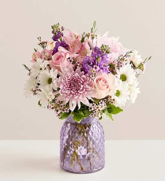Timeless Beauty Bouquet - Some gifts speak louder than words — and the Timeless Beauty Bouquet says it all with grace, color, and elegance. Thoughtfully handcrafted by our expert florists, this radiant arrangement is perfect for any occasion: a heartfelt thank you, a cheerful birthday wish, or a simple &quot;thinking of you.&quot;  Brimming with soft pink roses, delicate pink alstroemerias, fragrant purple stock, and cheerful white daisies, each bloom is chosen to evoke warmth, joy, and timeless beauty. The flowers are artfully arranged in a lavender glass vase, adding a touch of refined charm that makes this bouquet a true standout.  From morning smiles to evening surprises, the Timeless Beauty Bouquet delivers love and light — no matter the moment.