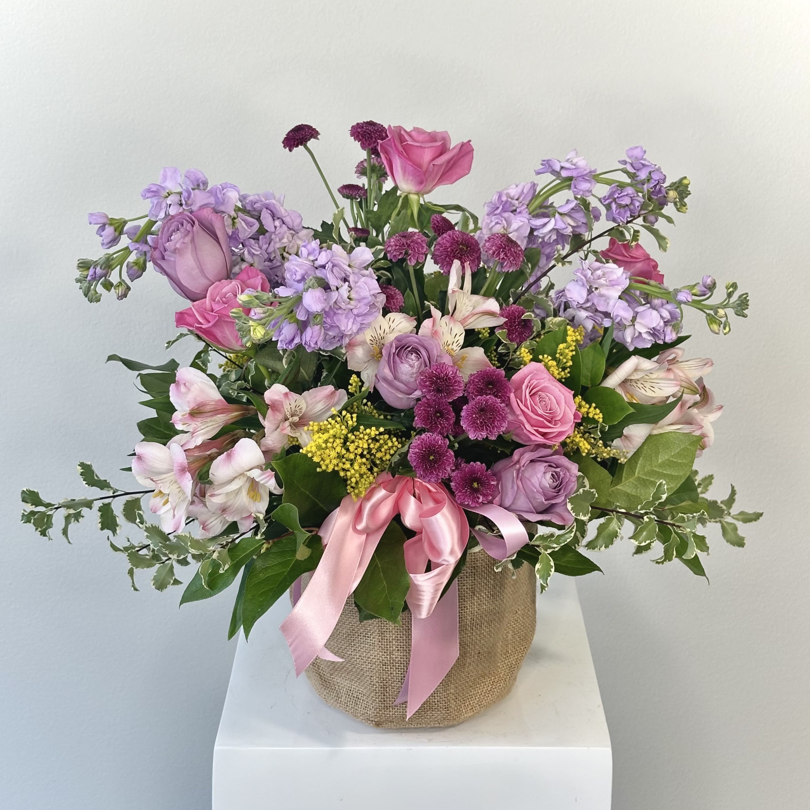 Basket of Love - Basket of Love: reminiscent of a day in nature picking wild flowers, this vintage design begins with a rustic basket that is filled with a whimsical collection of field-grown flowers. Main colors: lavender, pink, purple, white. Typically includes: Lavender Roses, Larkspur, Lavender Daisies, White Daisies, Purple Cushions, Green Cushions, Wax Flower, Silver Dollar Eucalyptus, Lisianthus, Aster Matsumoto. Subject to substitution.