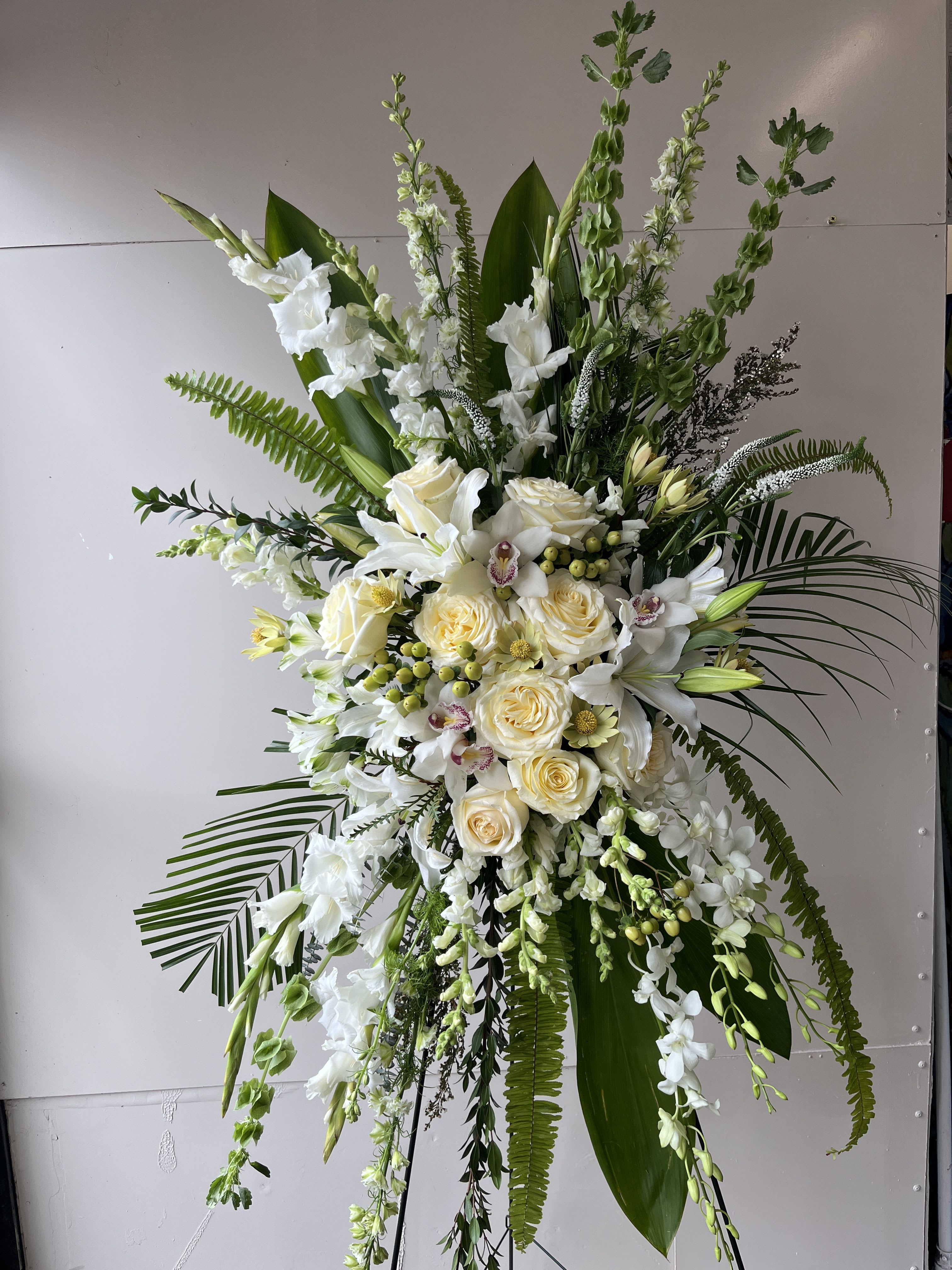 Heaven's Embrace Heaven's Embrace - A timeless tribute of peace and purity, Heaven’s Embrace features cascading white orchids, roses, lilies, and gladiolus, accented with lush greenery and delicate tropical leaves. Designed to convey love, remembrance, and grace, this standing arrangement brings comfort and beauty to moments of farewell.