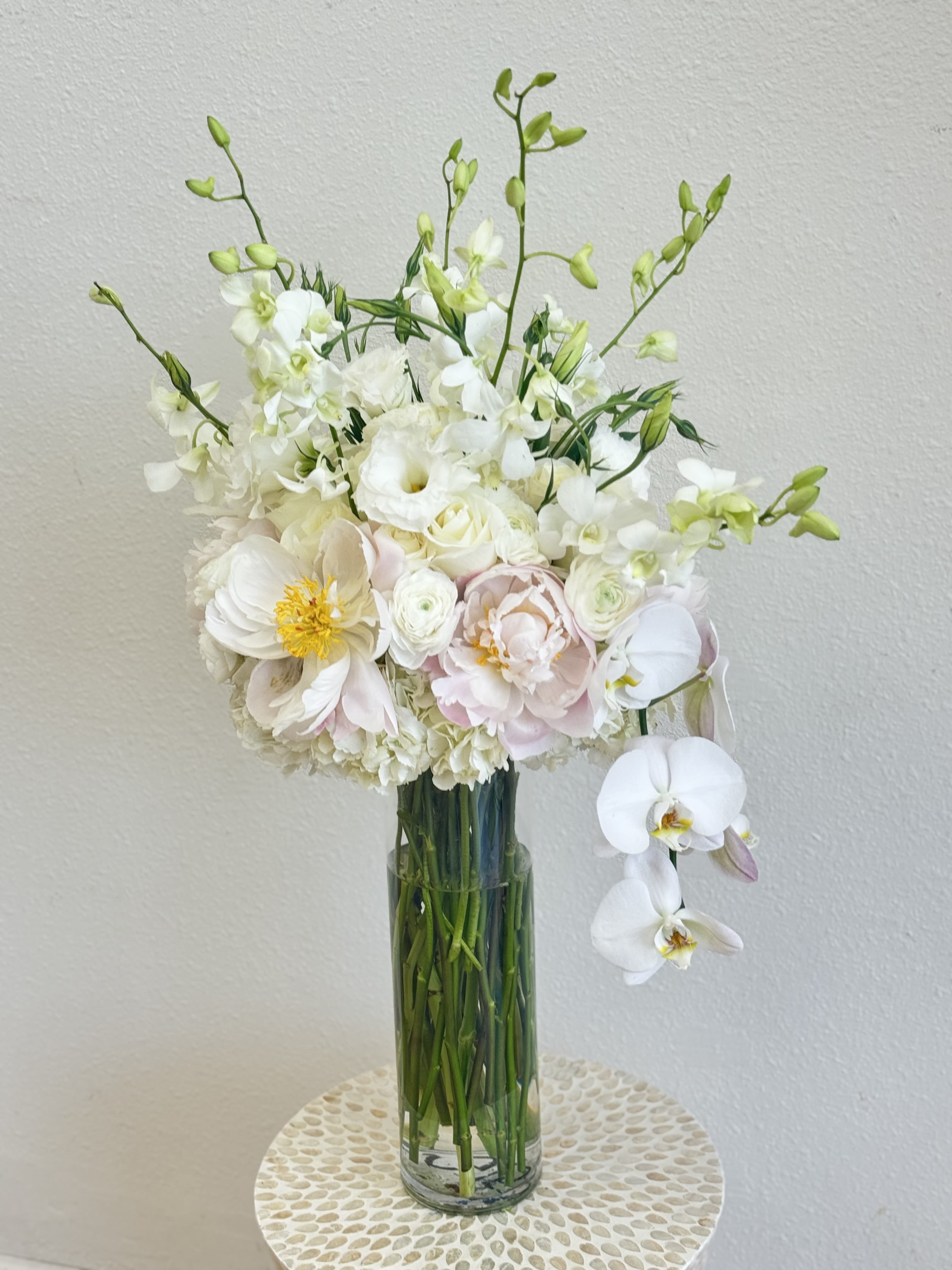 Graceful Elegance Vase Arrangement - Timeless and refined, the Graceful Elegance arrangement brings a touch of serenity and luxury to any space. This sophisticated design features white orchids, lisianthus, dendrobium blooms, soft blush peonies, roses, and hydrangeas — all arranged in a tall clear glass vase. Perfect for weddings, sympathy gestures, anniversaries, or upscale events, this bouquet speaks with quiet beauty and grace.  Available for flower delivery in Los Angeles.