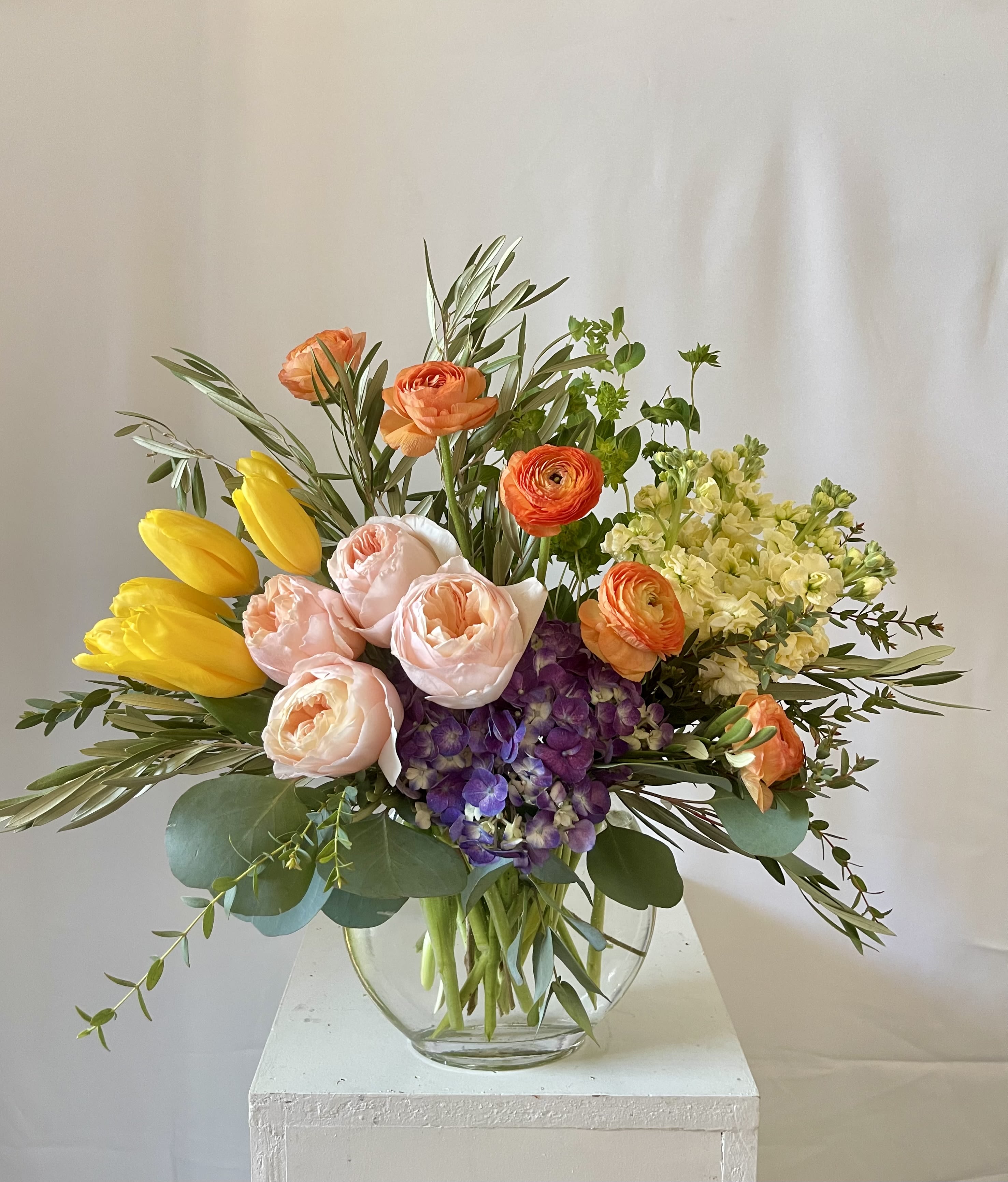 Sunset Splendor - Inspired by the rich, glowing colors of a perfect sunset, Sunset Splendor is a joyful mix of seasonal blooms that radiate warmth and beauty. Featuring lush purple hydrangeas, sunny yellow stock, cheerful yellow tulips, soft pink garden roses, and delicate ranunculus, all accented with fresh mixed greenery, this arrangement is a celebration of color and life.  Handcrafted by Julia’s Floral and available for same-day flower delivery in Dallas, it’s the perfect choice to brighten any space or send a heartfelt message full of joy and color.